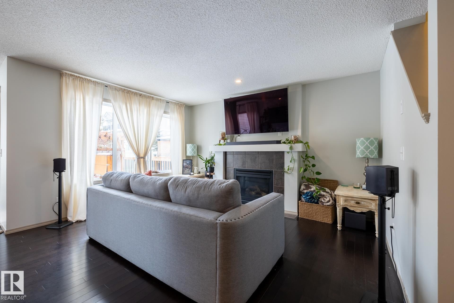 Living area featuring dark wood-type flooring, a tiled fireplace, and a textured ceiling - 3312 17B Avenue, Edmonton, AB - Indoor Photo Showing Living Room With Fireplace