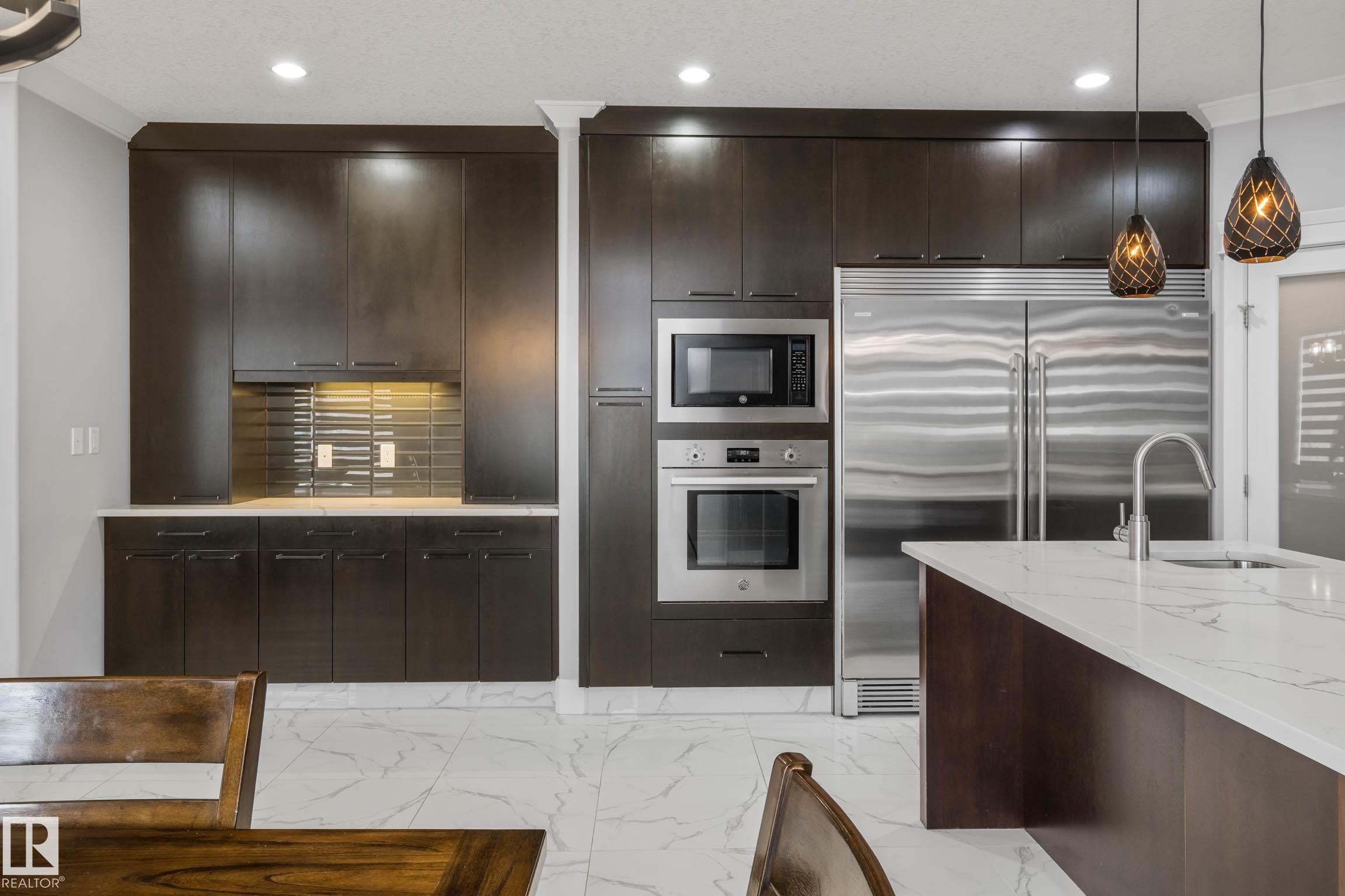 Kitchen featuring built in appliances, dark wood finish cabinets, ornamental molding, light marble finish flooring, and pendant lighting - 4086 Whispering River Drive, Edmonton, AB - Indoor Photo Showing Kitchen With Stainless Steel Kitchen With Upgraded Kitchen
