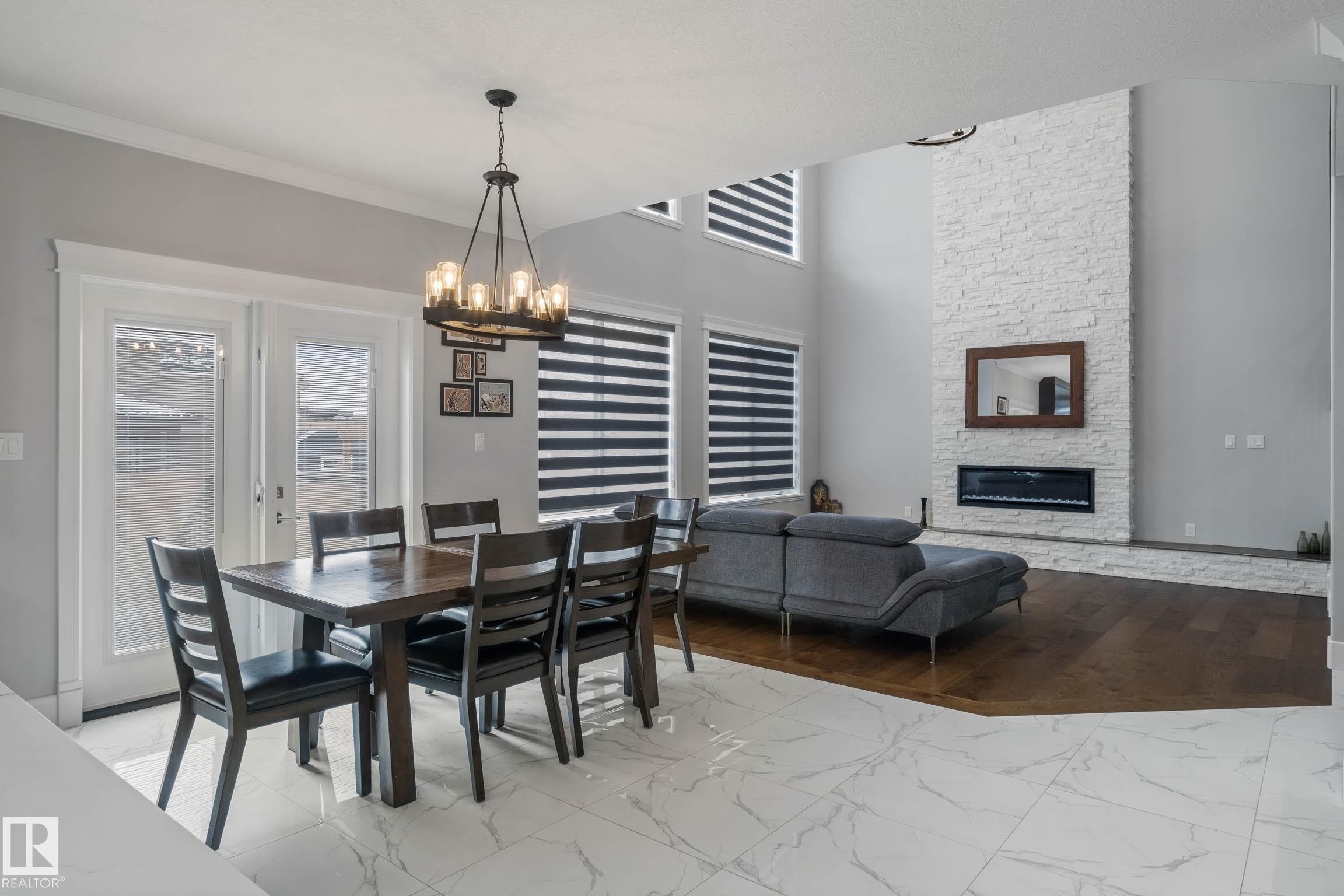 Dining room featuring marble look tile flooring, a stone fireplace, healthy amount of natural light, suspended lighting, and a high ceiling - 4086 Whispering River Drive, Edmonton, AB - Indoor Photo Showing Dining Room With Fireplace