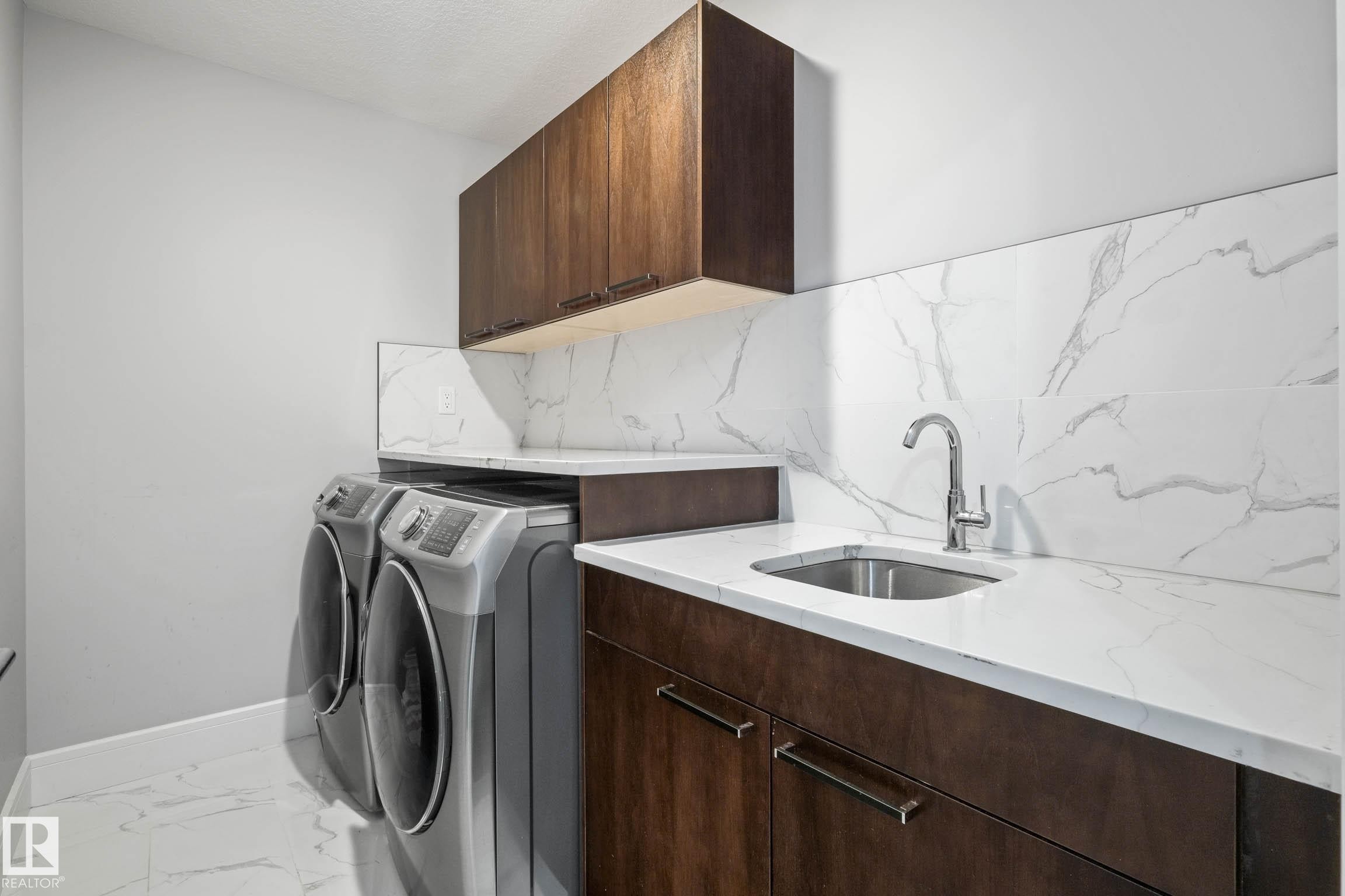 Laundry area featuring cabinet space, washing machine and dryer, and light marble finish floors - 4086 Whispering River Drive, Edmonton, AB - Indoor Photo Showing Laundry Room