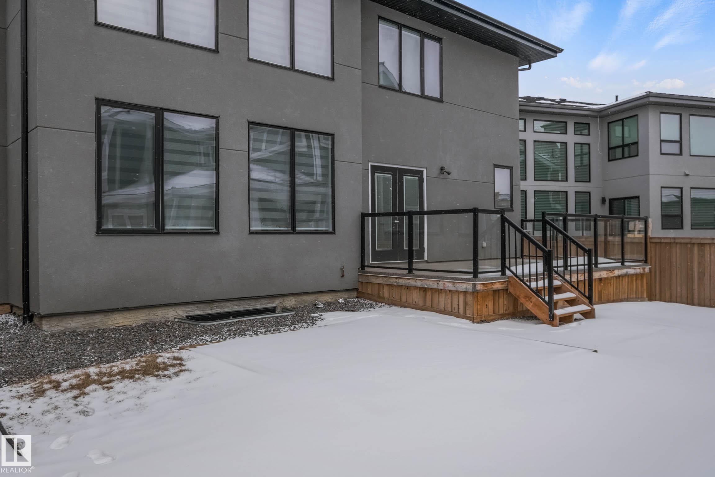 Snow covered property featuring stucco siding, a patio, and a wooden deck - 4086 Whispering River Drive, Edmonton, AB - Outdoor