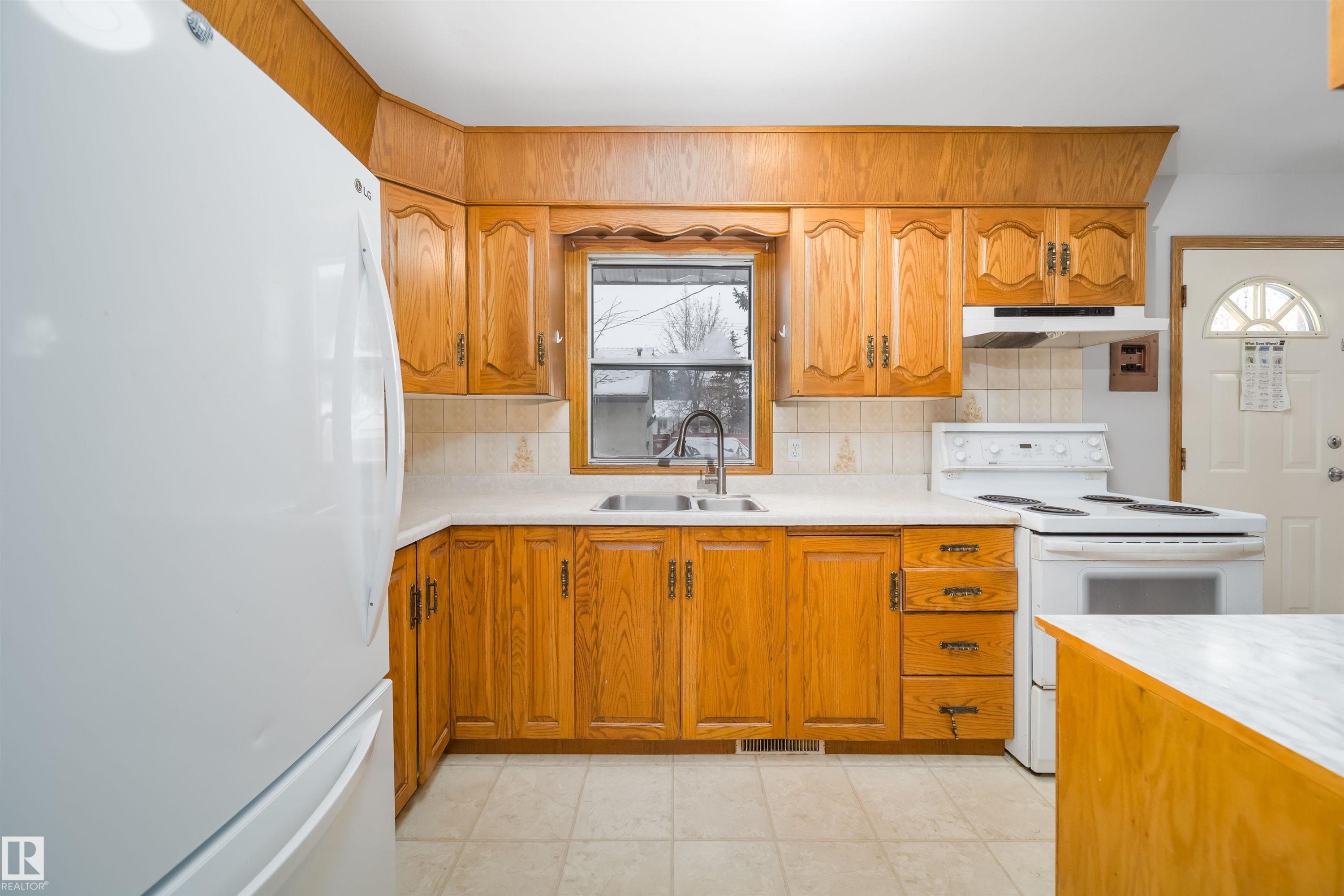 Kitchen featuring white appliances, light countertops, wood finish cabinets, and tasteful backsplash - 8908 130 Avenue Nw, Edmonton, AB - Indoor Photo Showing Kitchen With Double Sink