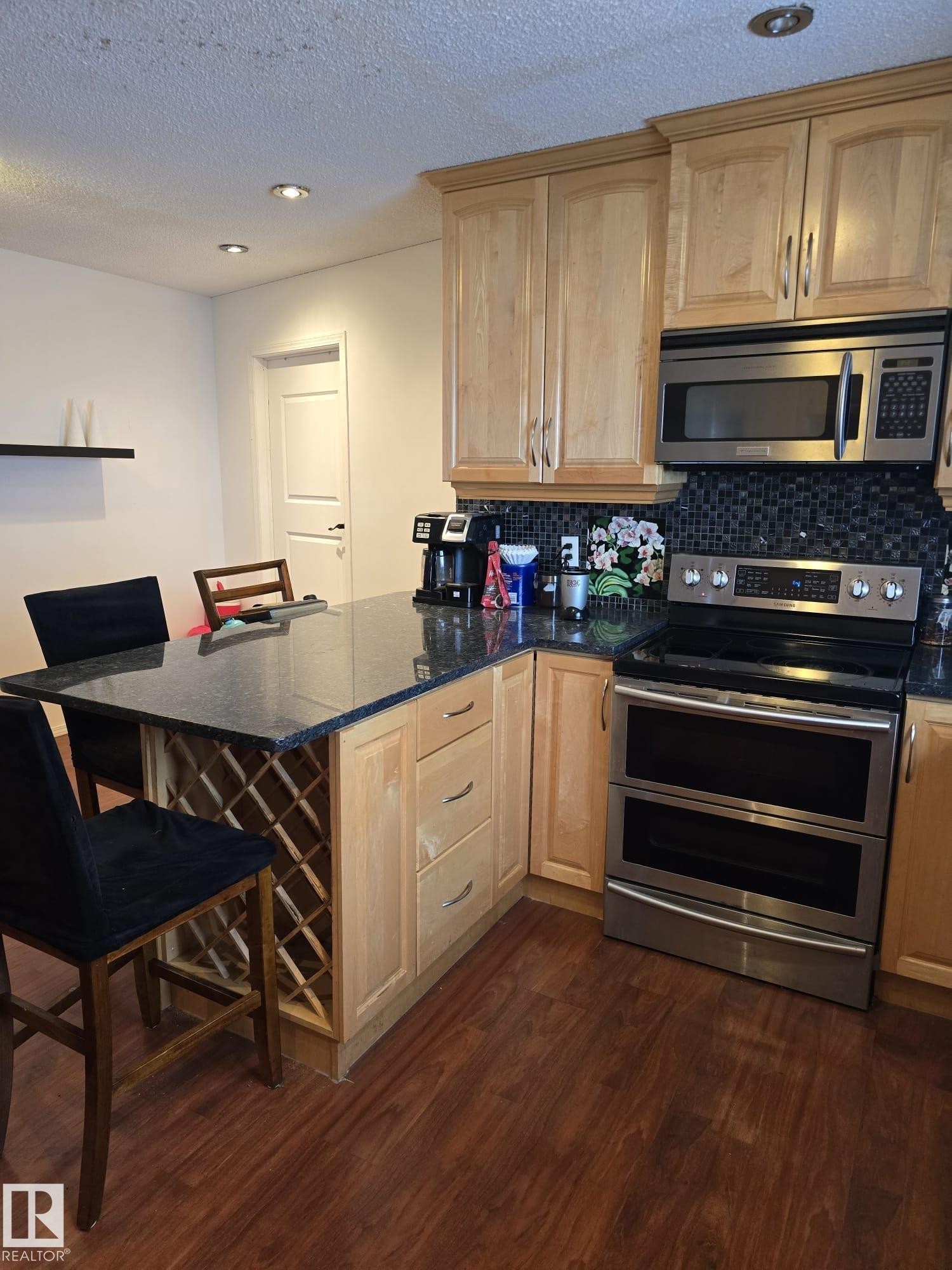Kitchen with stainless steel appliances, a peninsula, a breakfast bar area, dark stone counters, and dark wood-style flooring - 11927 85 Street Nw, Edmonton, AB - Indoor Photo Showing Kitchen