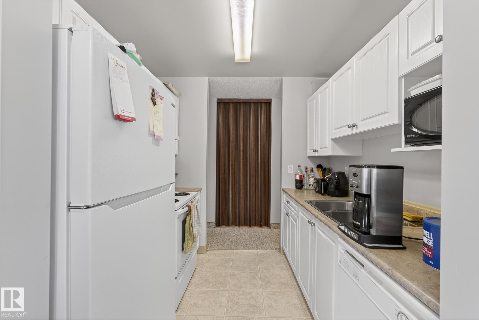Kitchen with white appliances, light countertops, white cabinetry, and light tile patterned flooring - 302 4608 52 Avenue, Stony Plain, AB - Indoor Photo Showing Kitchen With Double Sink