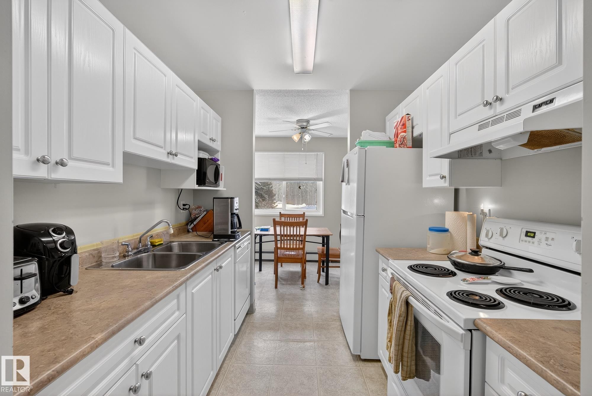 Kitchen featuring white appliances, white cabinetry, light countertops, and ceiling fan - 302 4608 52 Avenue, Stony Plain, AB - Indoor Photo Showing Kitchen With Double Sink