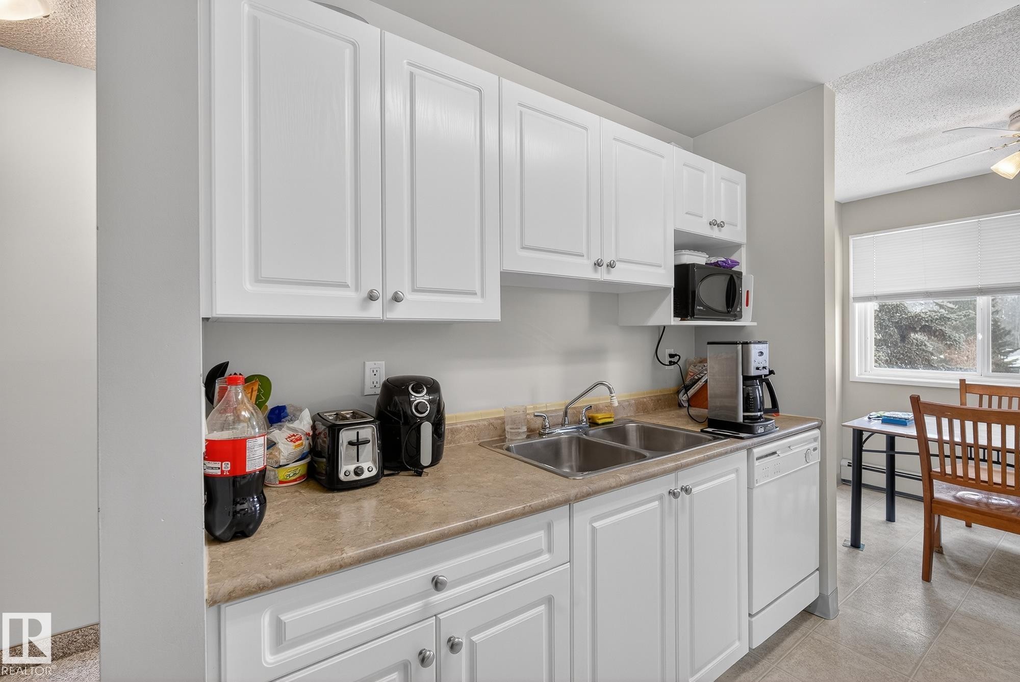 Kitchen featuring a textured ceiling, white cabinetry, light countertops, white dishwasher, and black microwave - 302 4608 52 Avenue, Stony Plain, AB - Indoor Photo Showing Kitchen With Double Sink