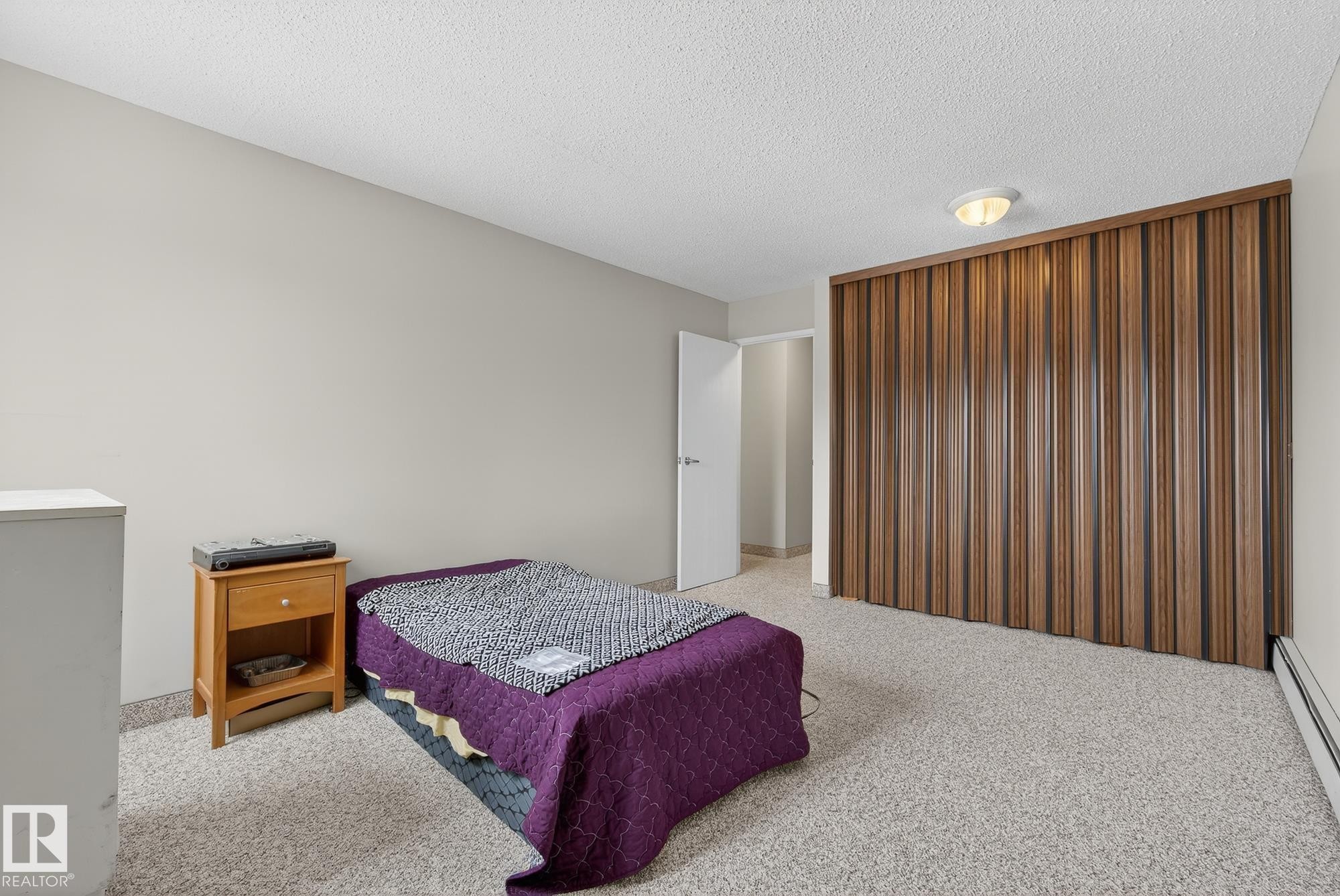 Bedroom featuring light colored carpet, a baseboard radiator, and a textured ceiling - 302 4608 52 Avenue, Stony Plain, AB - Indoor Photo Showing Bedroom