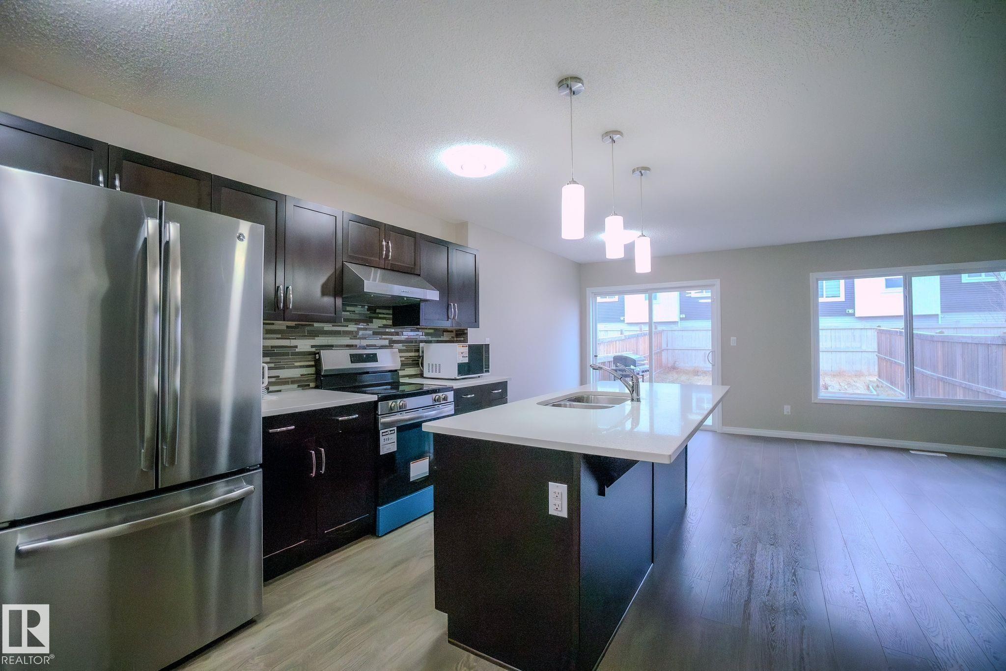 Kitchen with stainless steel appliances, a kitchen island with sink, pendant lighting, a textured ceiling, and backsplash - Edmonton, AB - Indoor Photo Showing Kitchen With Double Sink With Upgraded Kitchen