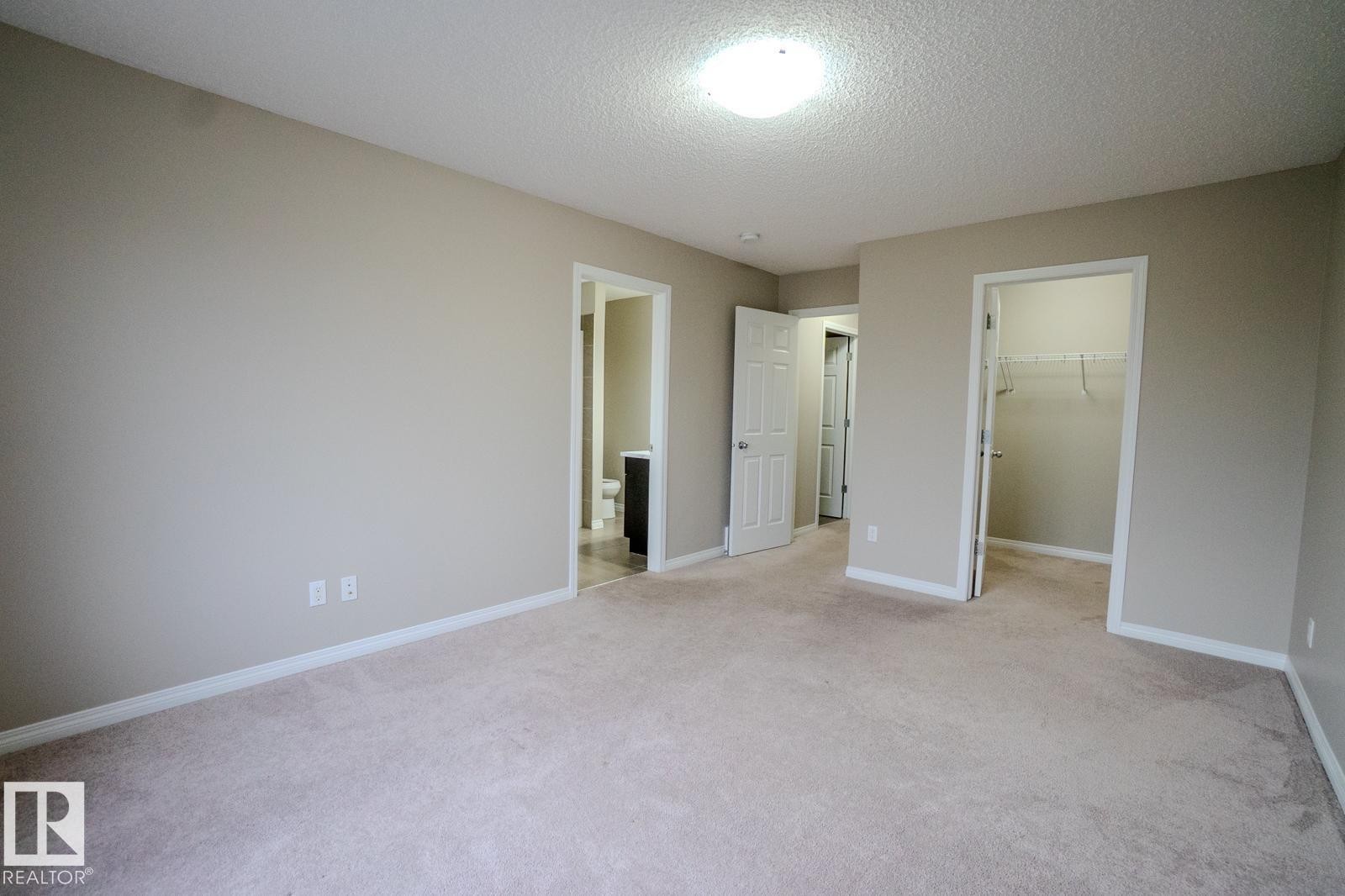 Unfurnished bedroom featuring a spacious closet, light colored carpet, a textured ceiling, and ensuite bath - Edmonton, AB - Indoor Photo Showing Other Room