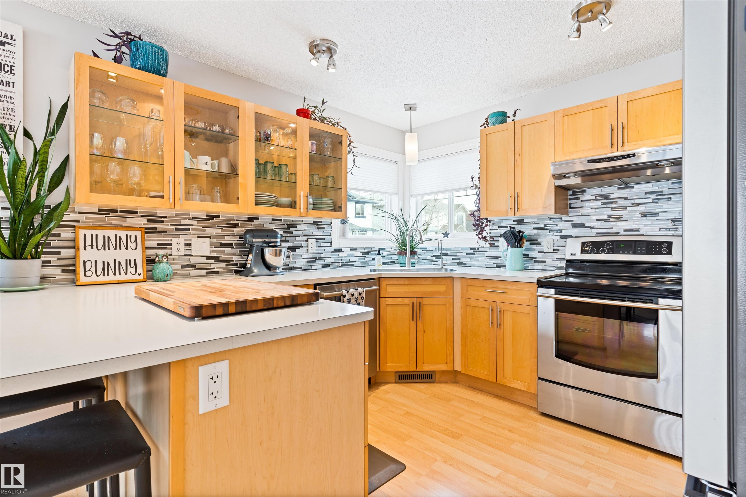 Kitchen with a kitchen breakfast bar, a peninsula, glass insert cabinets, light countertops, and stainless steel appliances - 7804 Schmid Place, Edmonton, AB - Indoor Photo Showing Kitchen With Double Sink