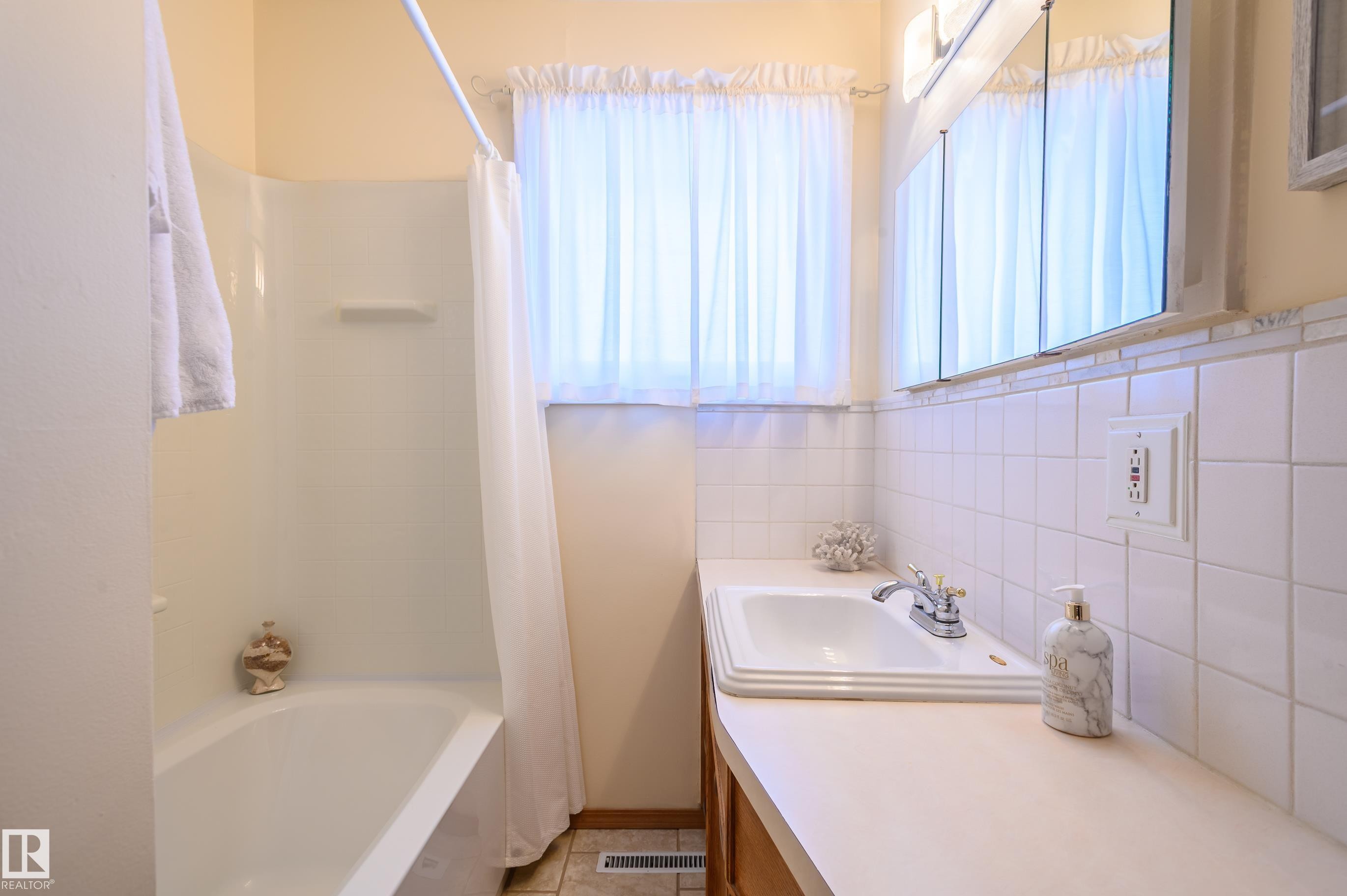 Bathroom featuring vanity, shower / bath combination with curtain, tile walls, and light tile patterned flooring - 13420 113A St, Edmonton, AB - Indoor Photo Showing Bathroom