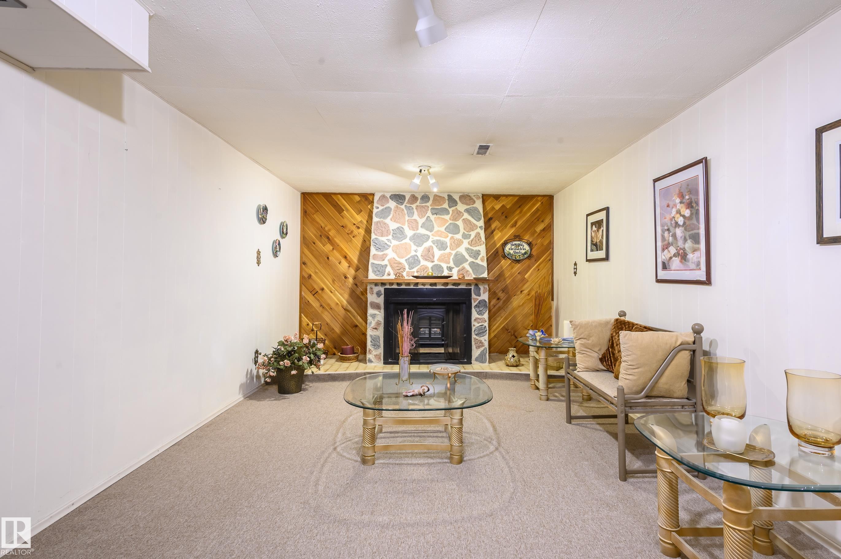 Carpeted living room featuring wood walls and a stone fireplace - 13420 113A St, Edmonton, AB - Indoor Photo Showing Living Room With Fireplace