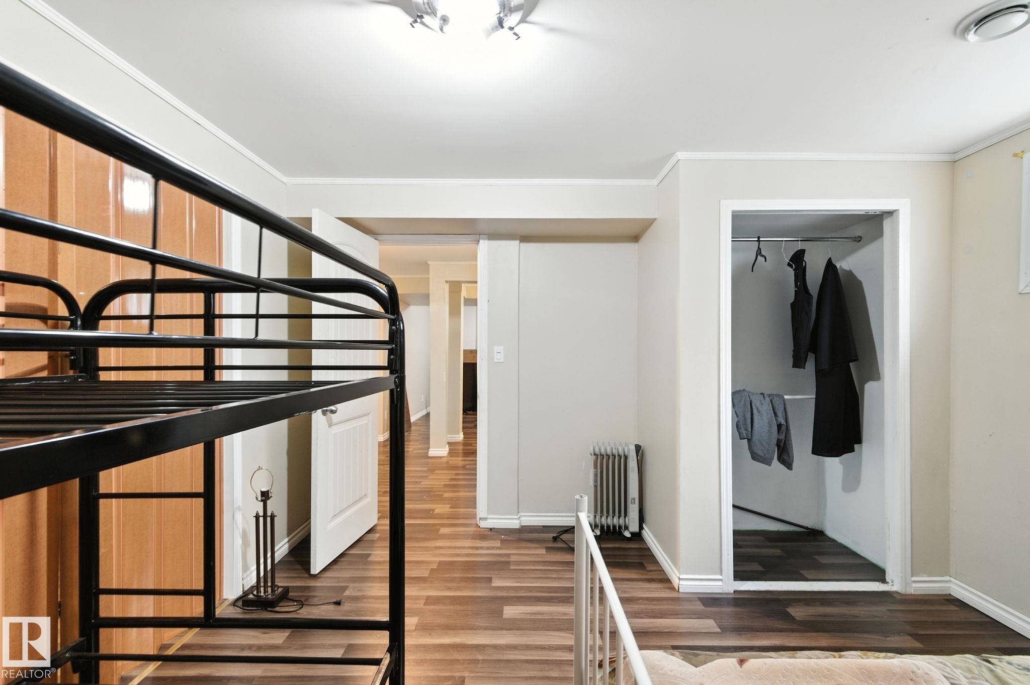 Unfurnished bedroom with wood finished floors, a closet, radiator heating unit, and ornamental molding - 7836 7 Avenue, Edmonton, AB - Indoor Photo Showing Other Room