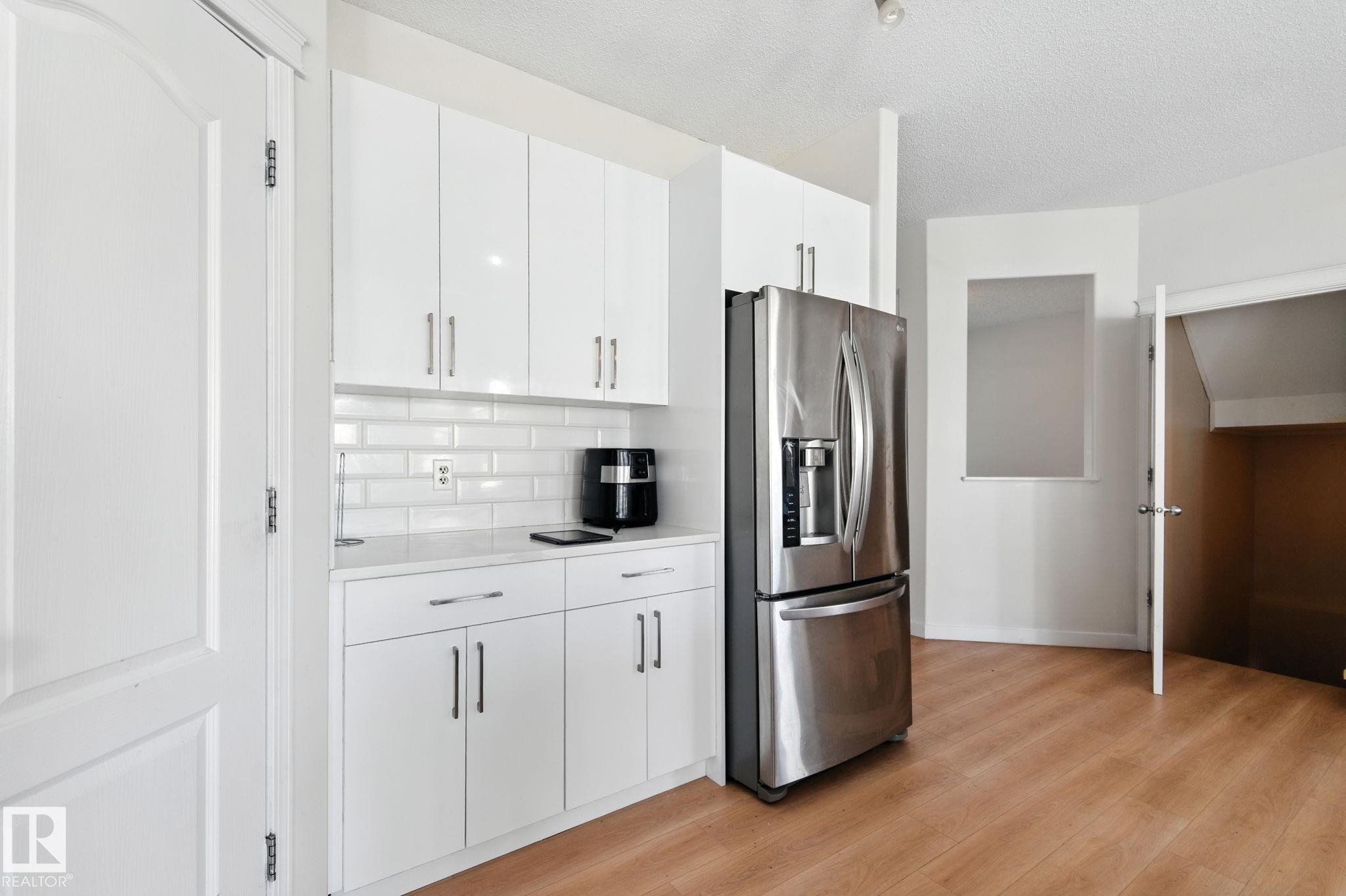 Kitchen with stainless steel fridge with ice dispenser, white cabinetry, light wood-style flooring, a textured ceiling, and tasteful backsplash - 7836 7 Avenue, Edmonton, AB - Indoor Photo Showing Kitchen