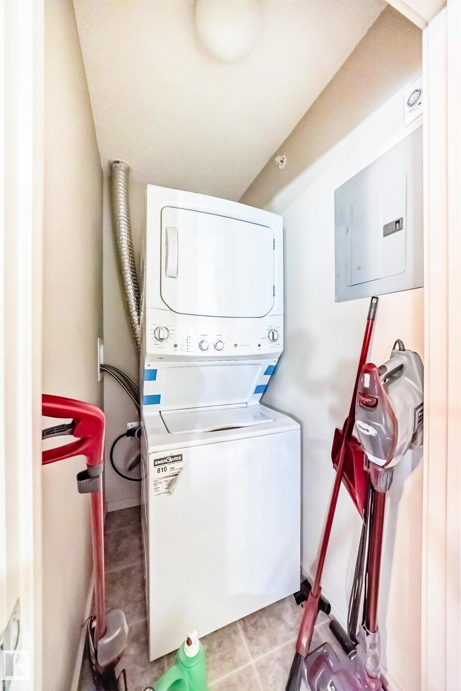 Laundry area featuring electric panel, stacked washer and dryer, and light tile patterned flooring - 403 340 Windermere Road, Edmonton, AB - Indoor Photo Showing Laundry Room