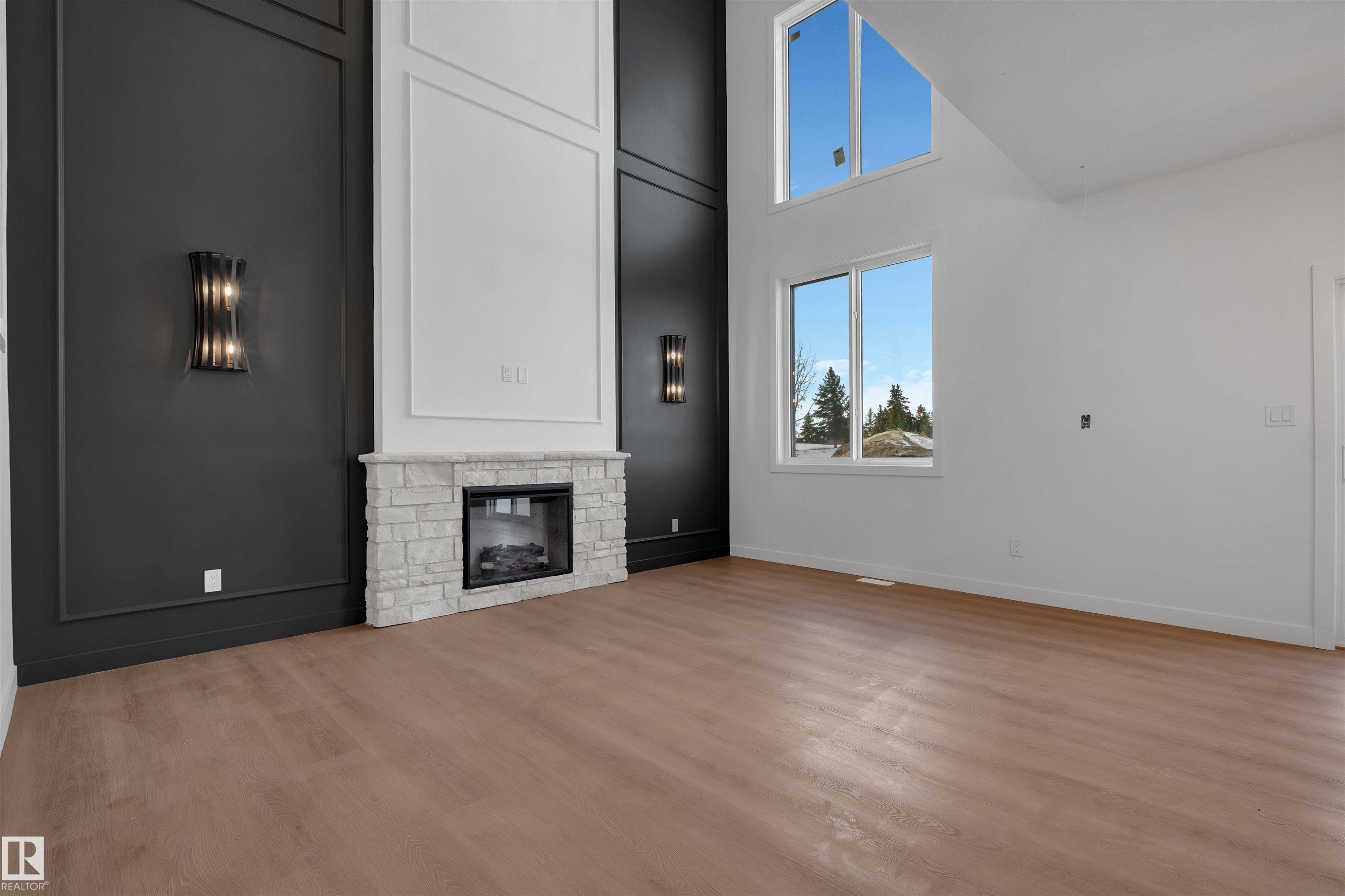 Unfurnished living room featuring a high ceiling, a fireplace, and light wood finished floors - 34 Grayson Green, Stony Plain, AB - Indoor With Fireplace