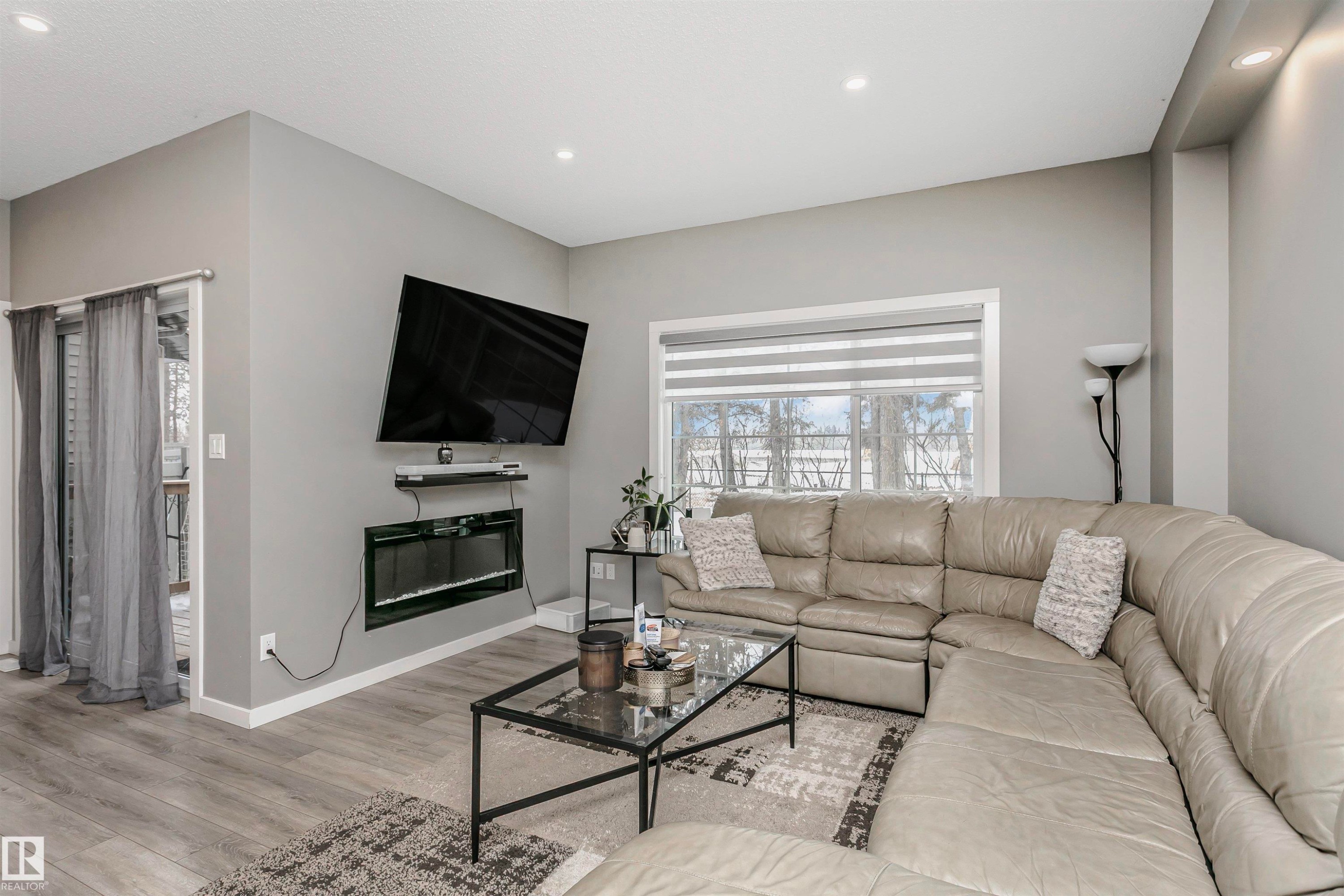 Living room with light wood-style floors, recessed lighting, and a glass covered fireplace - 7322 Chivers Crescent, Edmonton, AB - Indoor Photo Showing Living Room With Fireplace