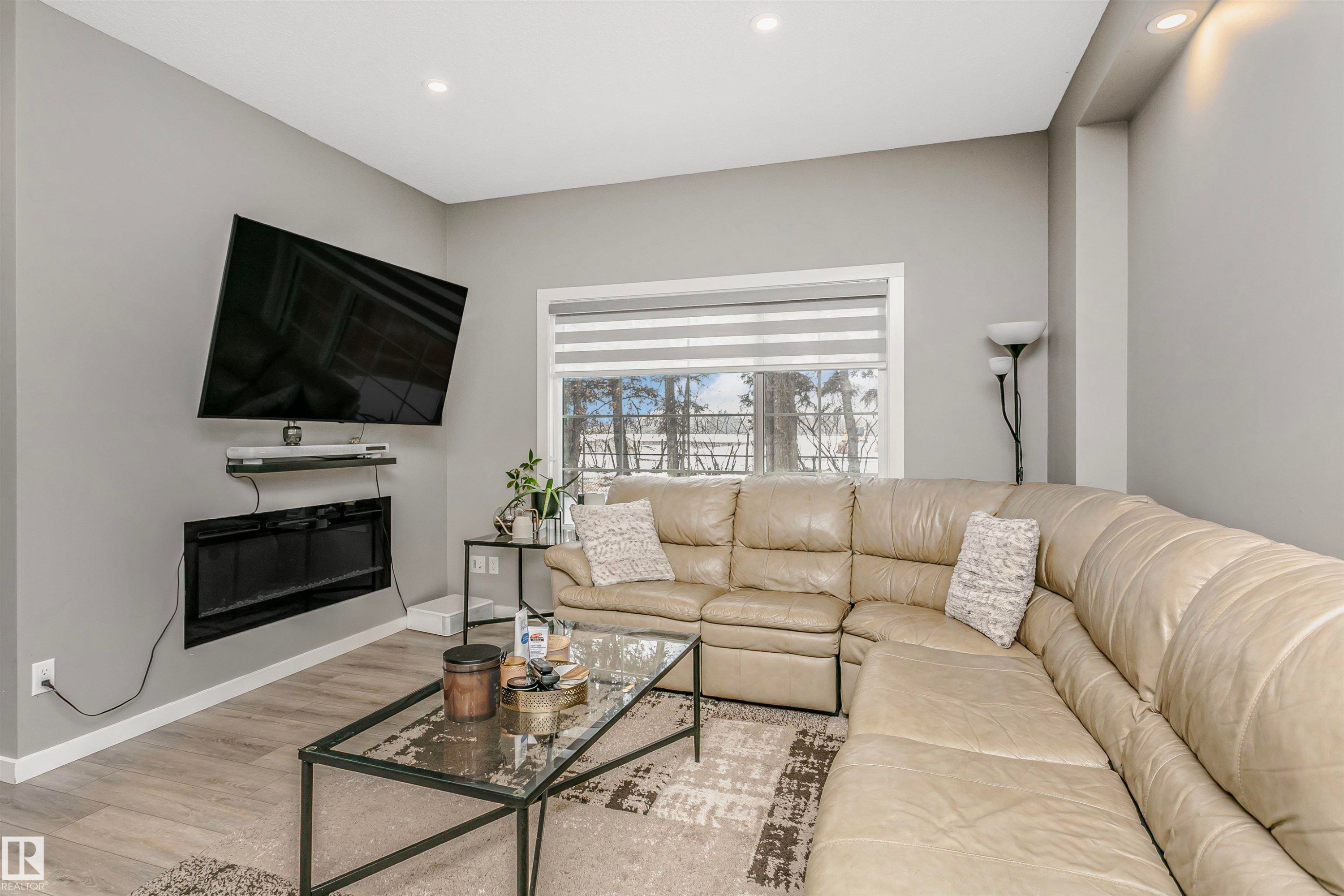 Living area featuring wood finished floors, a glass covered fireplace, and recessed lighting - 7322 Chivers Crescent, Edmonton, AB - Indoor Photo Showing Living Room With Fireplace