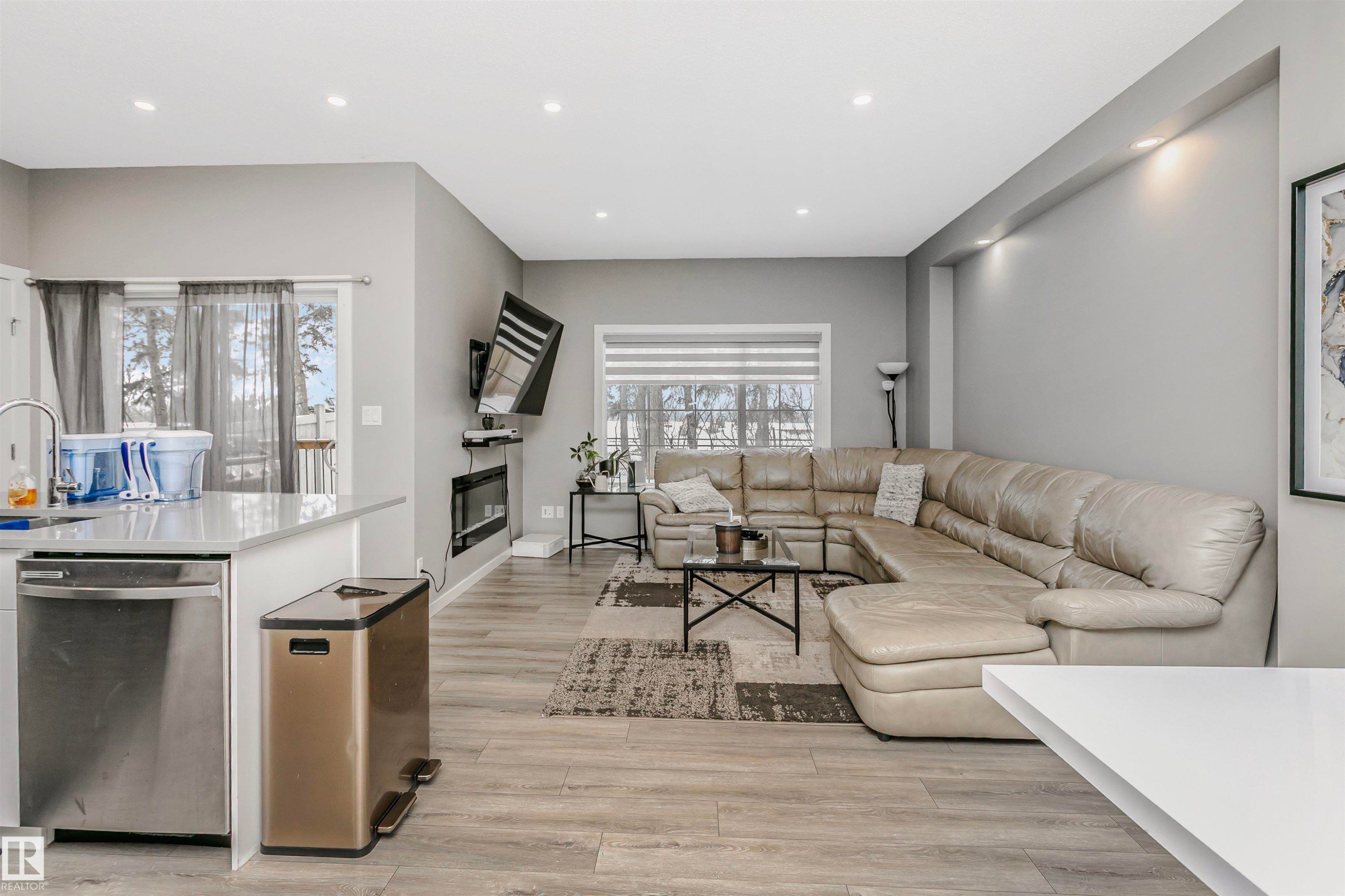 Living area with light wood finished floors, recessed lighting, and a glass covered fireplace - 7322 Chivers Crescent, Edmonton, AB - Indoor Photo Showing Living Room
