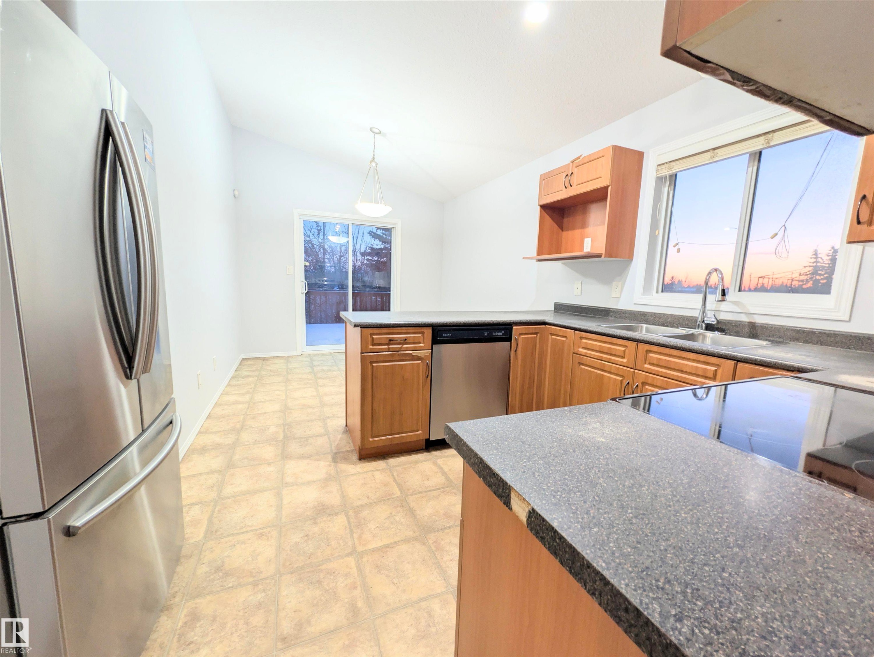 Kitchen featuring stainless steel appliances, dark countertops, lofted ceiling, a peninsula, and pendant lighting - 3307 24 Avenue, Edmonton, AB - Indoor Photo Showing Kitchen With Double Sink