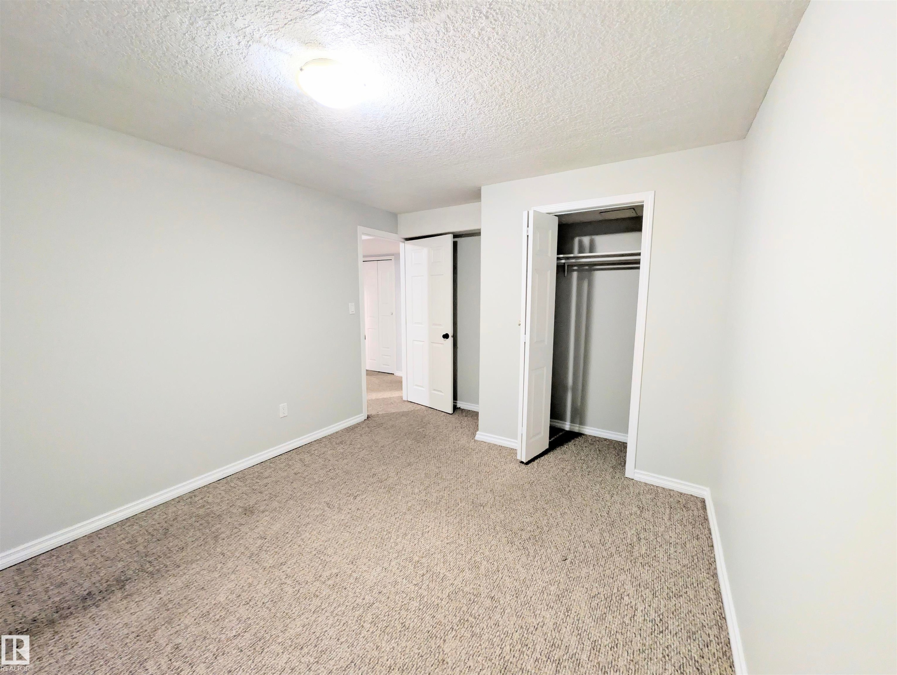 Unfurnished bedroom featuring a textured ceiling, a closet, and light carpet - 3307 24 Avenue, Edmonton, AB - Indoor Photo Showing Other Room