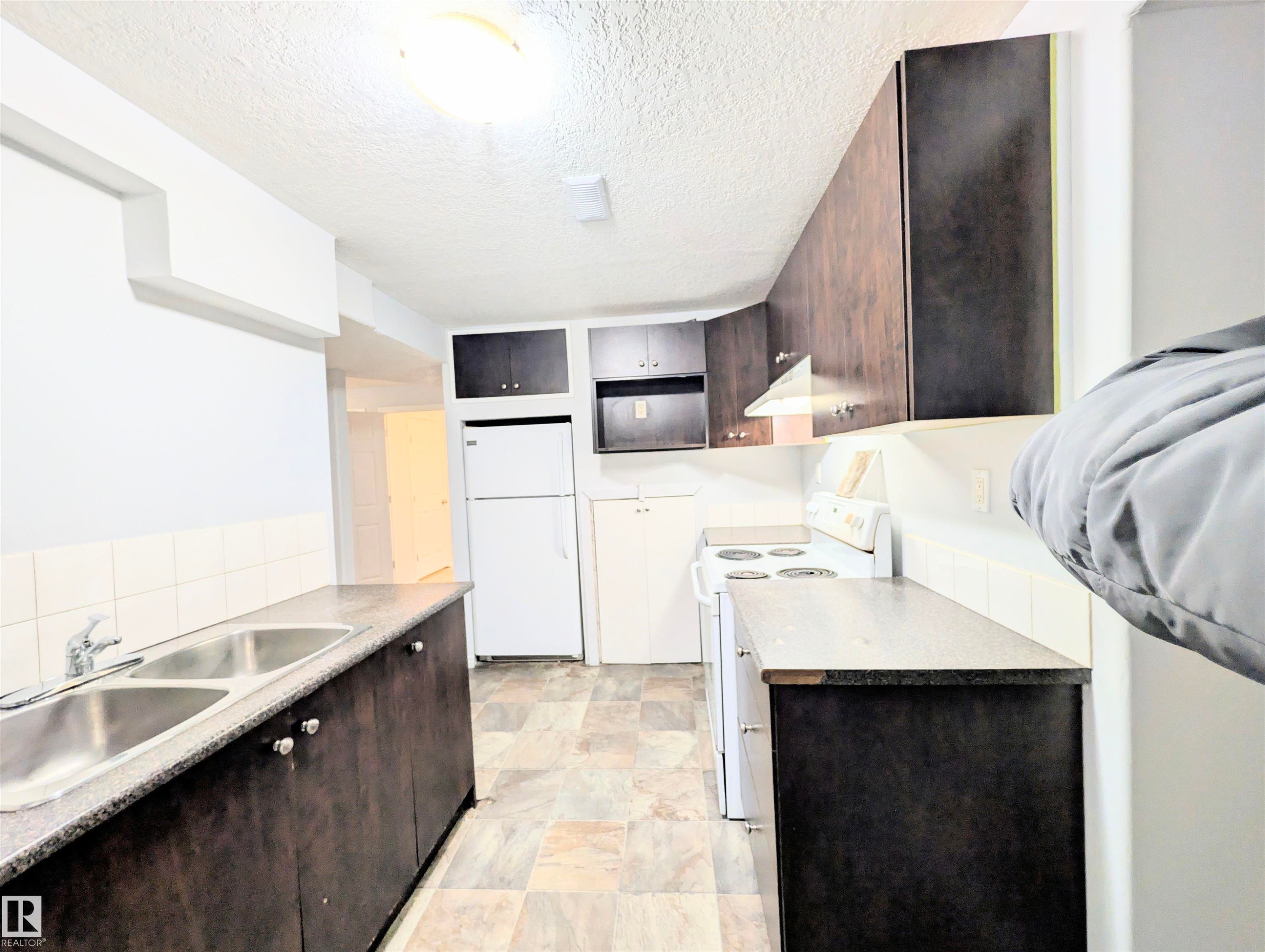 Kitchen with dark wood finish cabinets, white appliances, a textured ceiling, and light countertops - 3307 24 Avenue, Edmonton, AB - Indoor Photo Showing Kitchen With Double Sink