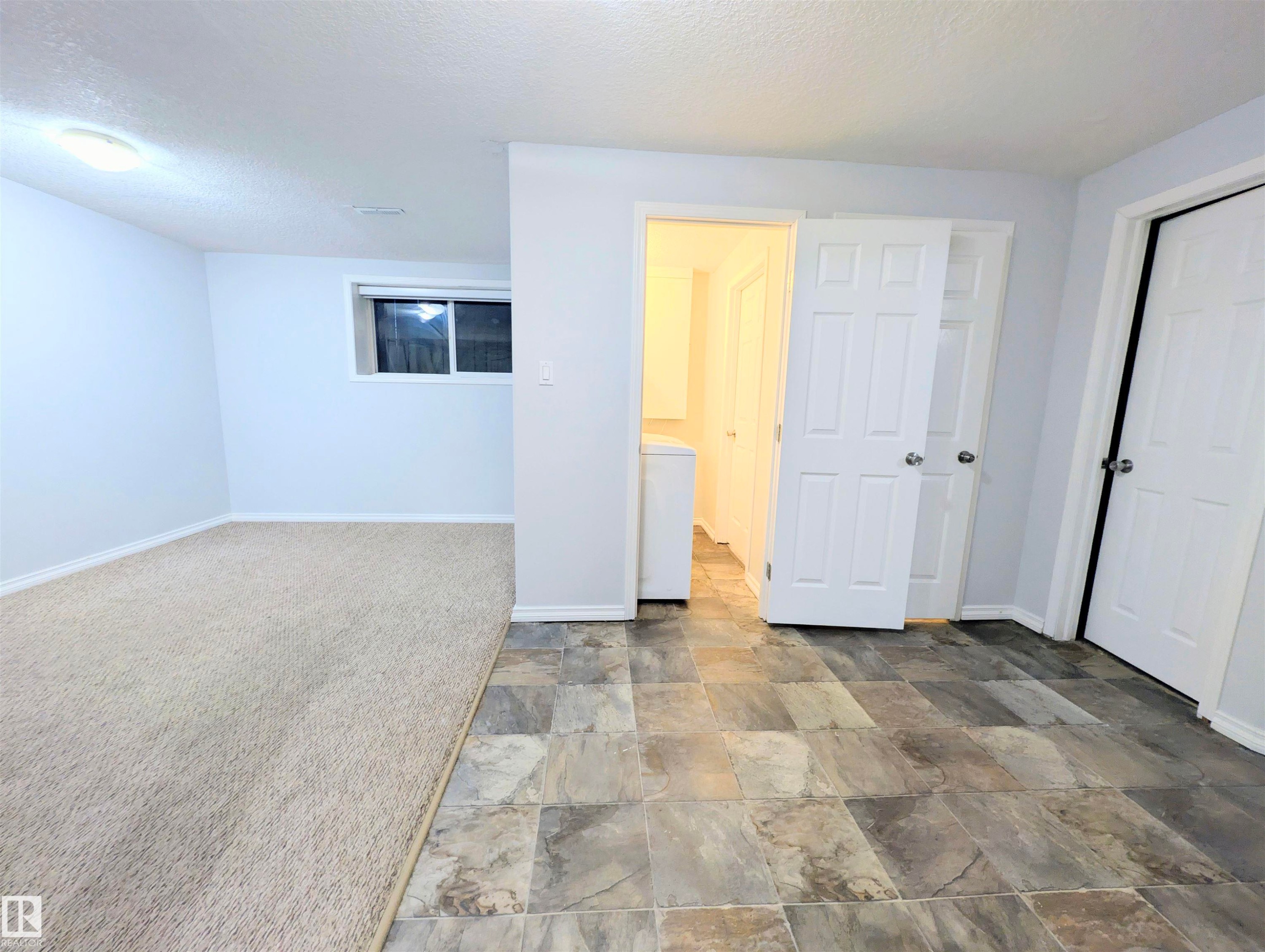 Unfurnished bedroom with stone finish floors, a textured ceiling, a closet, washer / dryer, and carpet flooring - 3307 24 Avenue, Edmonton, AB - Indoor Photo Showing Other Room