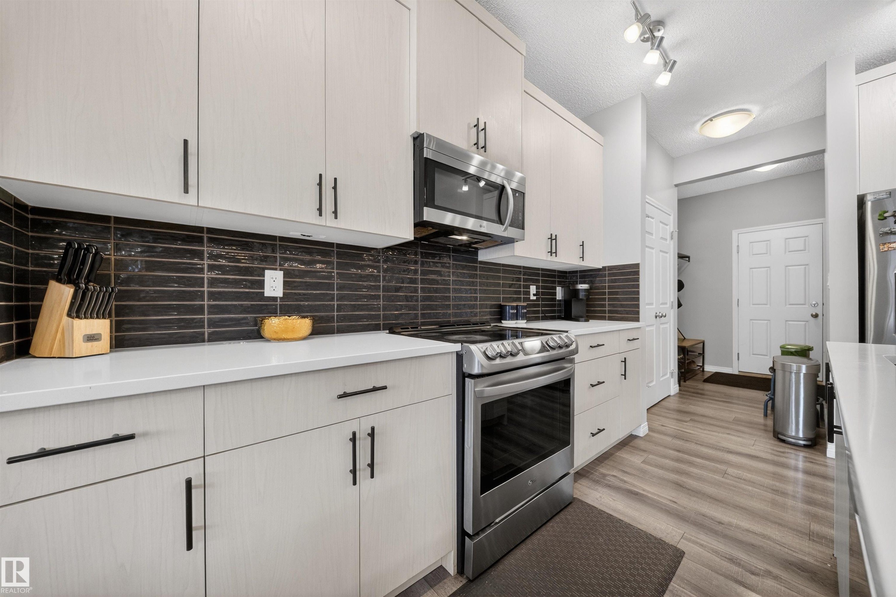 Kitchen with stainless steel appliances, light wood-style floors, decorative backsplash, a textured ceiling, and light stone countertops - 6085 King Landing, Edmonton, AB - Indoor Photo Showing Kitchen With Upgraded Kitchen
