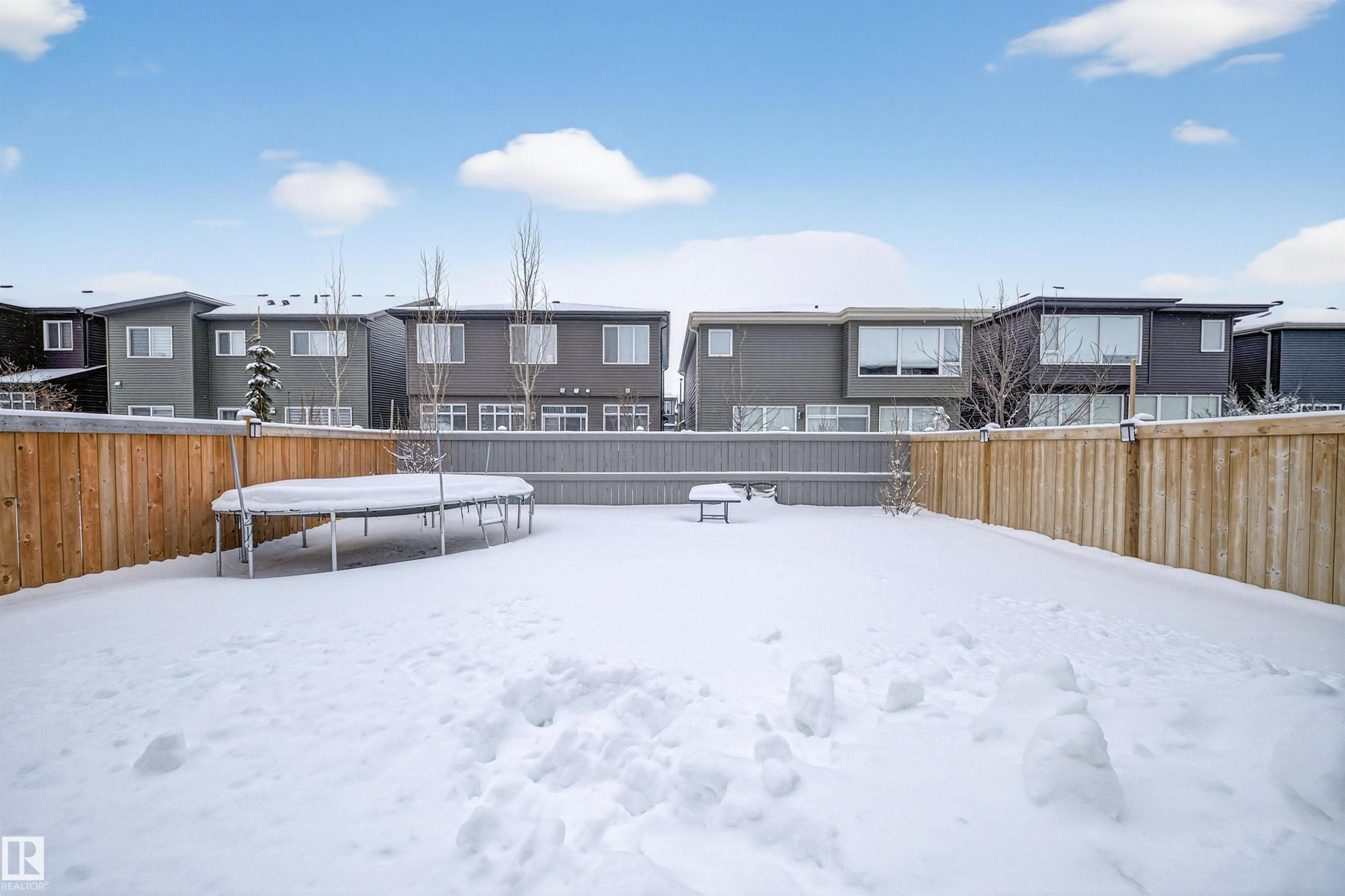 Snow covered rear of property featuring a trampoline, a fenced backyard, and a residential view - 6085 King Landing, Edmonton, AB - Outdoor