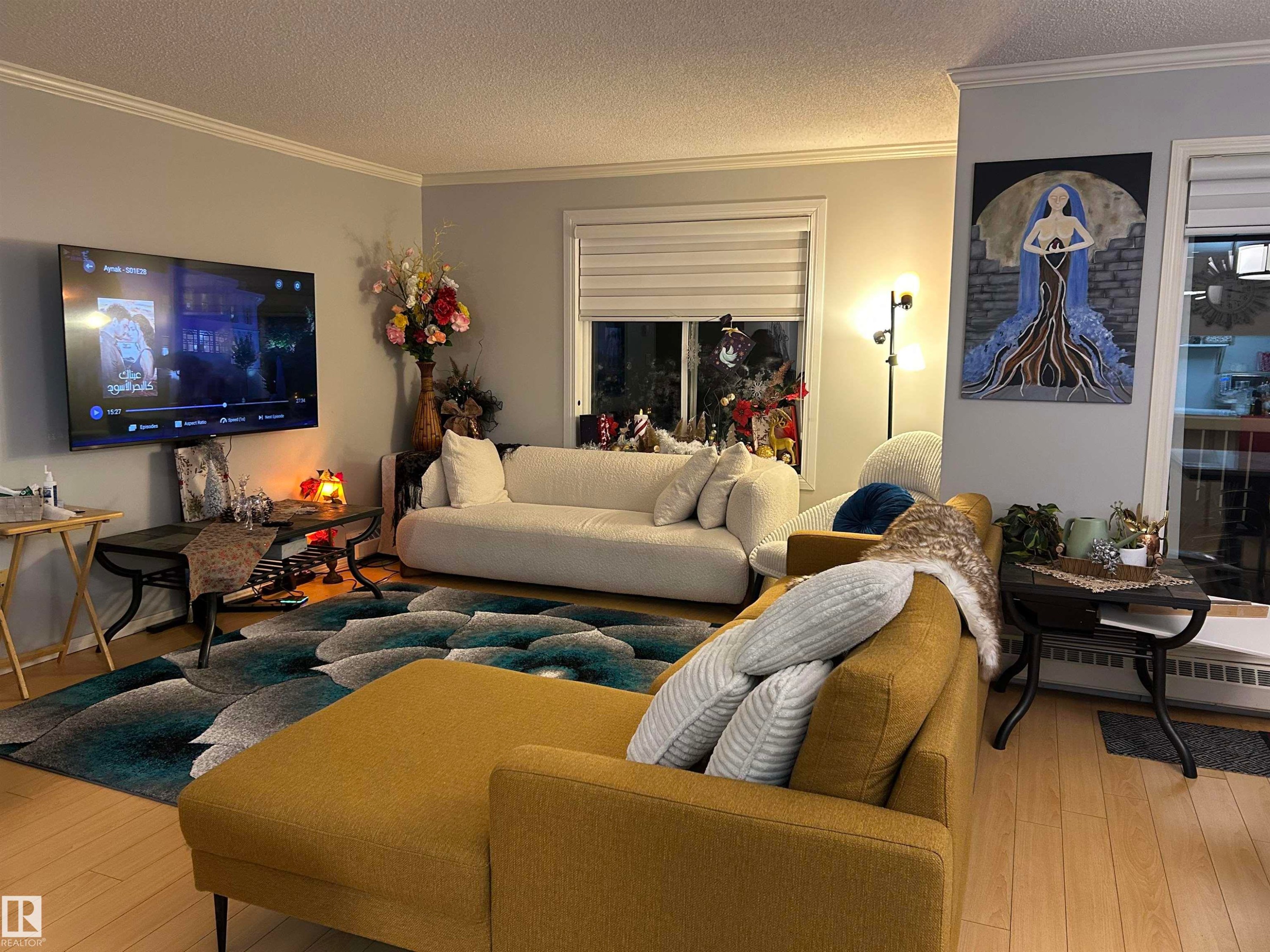 Living area featuring a textured ceiling, crown molding, wood-type flooring, and a baseboard radiator - 202 18020 95 Avenue, Edmonton, AB - Indoor Photo Showing Living Room