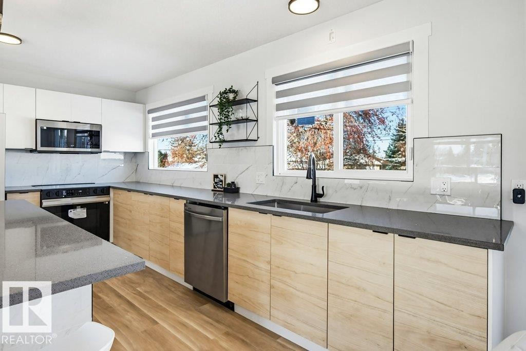 Kitchen with modern cabinets, dark stone counters, stainless steel appliances, backsplash, and light wood-type flooring - 7016 92A Avenue, Edmonton, AB - Indoor Photo Showing Kitchen
