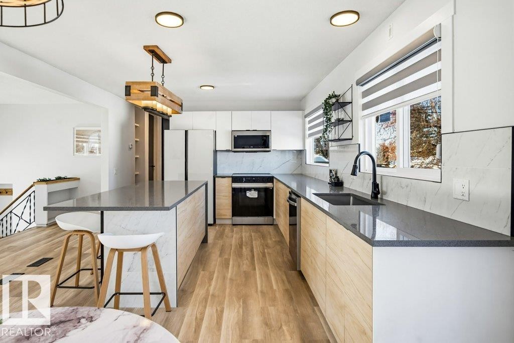 Kitchen featuring a breakfast bar area, dark stone counters, backsplash, decorative light fixtures, and white cabinetry - 7016 92A Avenue, Edmonton, AB - Indoor Photo Showing Kitchen With Upgraded Kitchen