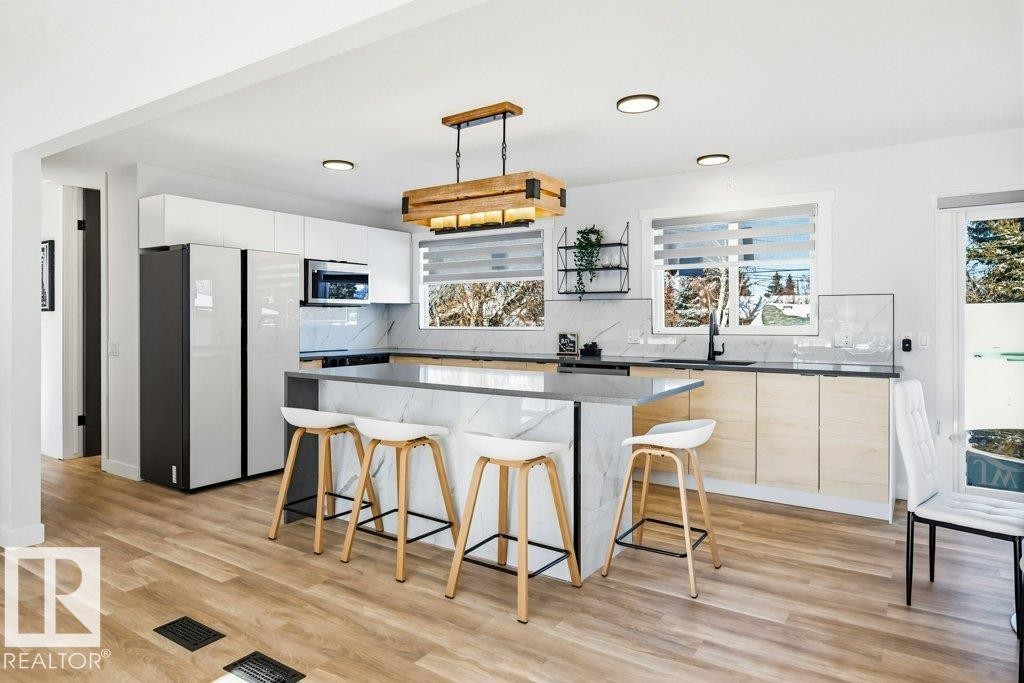 Kitchen featuring a breakfast bar area, a kitchen island, light wood-style flooring, pendant lighting, and freestanding refrigerator - 7016 92A Avenue, Edmonton, AB - Indoor