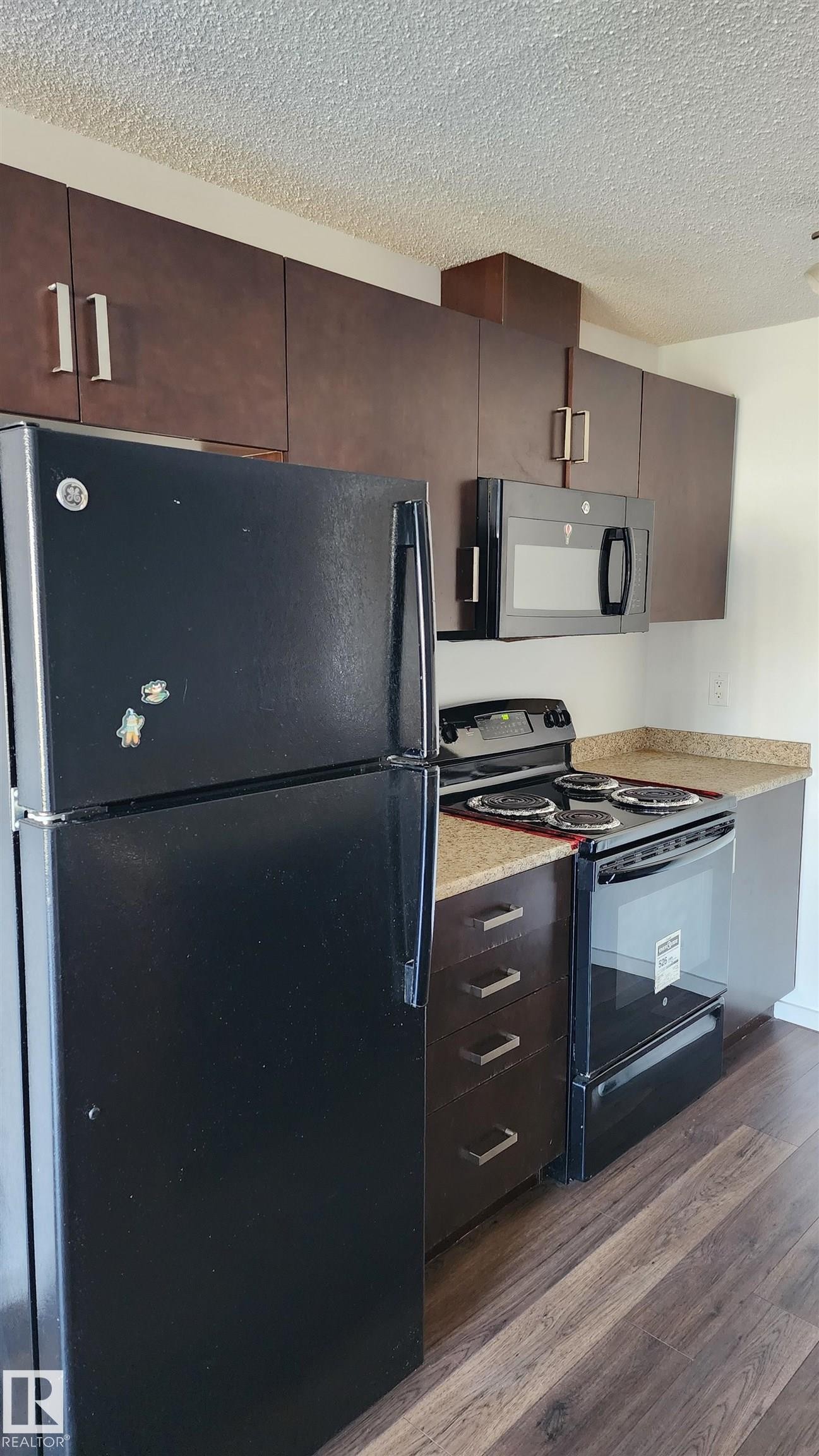Kitchen with black appliances, a textured ceiling, dark wood-style floors, dark wood finish cabinets, and modern cabinets - 413 5521 7 Avenue, Edmonton, AB - Indoor Photo Showing Kitchen