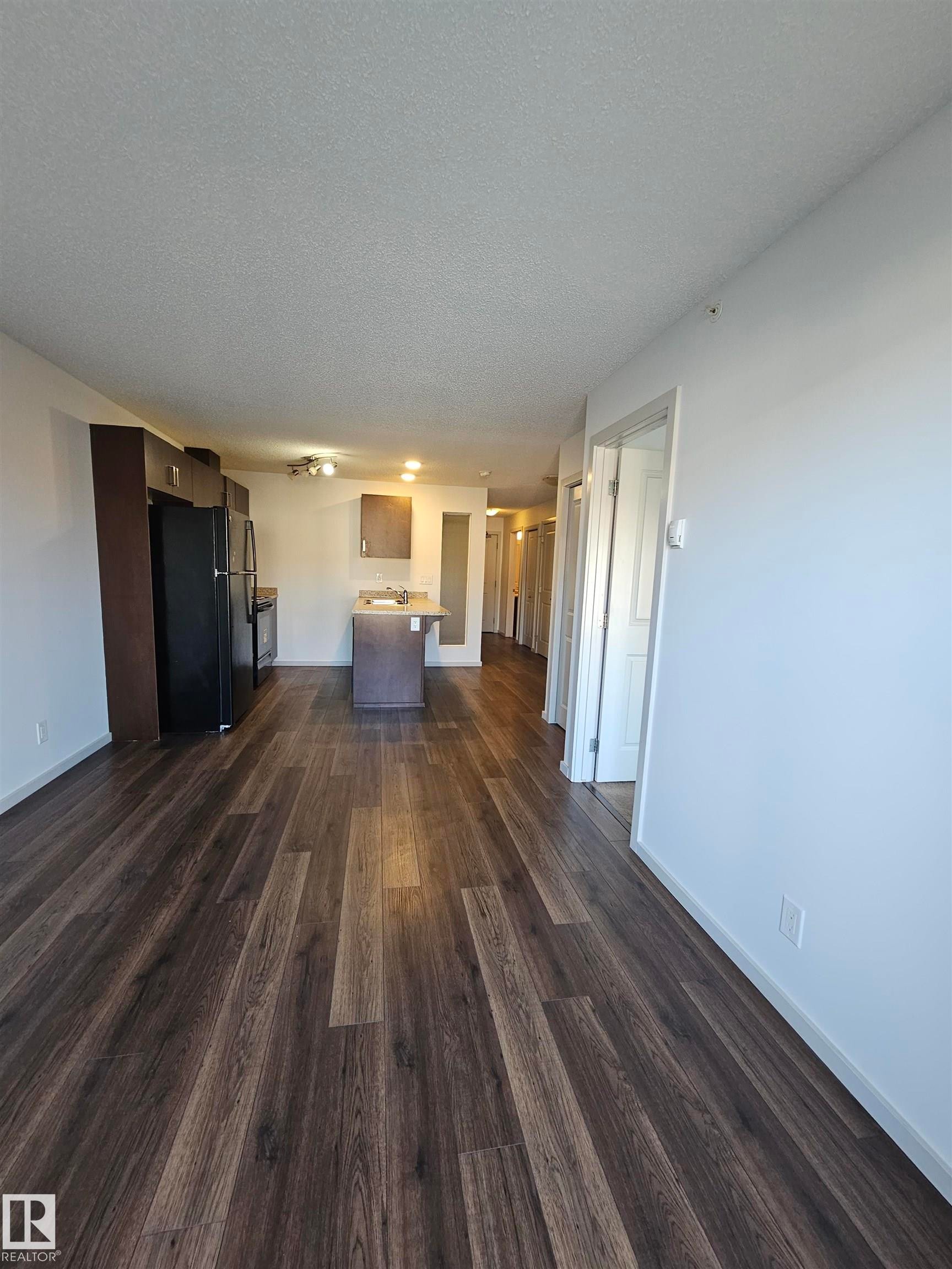 Unfurnished living room featuring dark wood-type flooring and a textured ceiling - 413 5521 7 Avenue, Edmonton, AB - Indoor