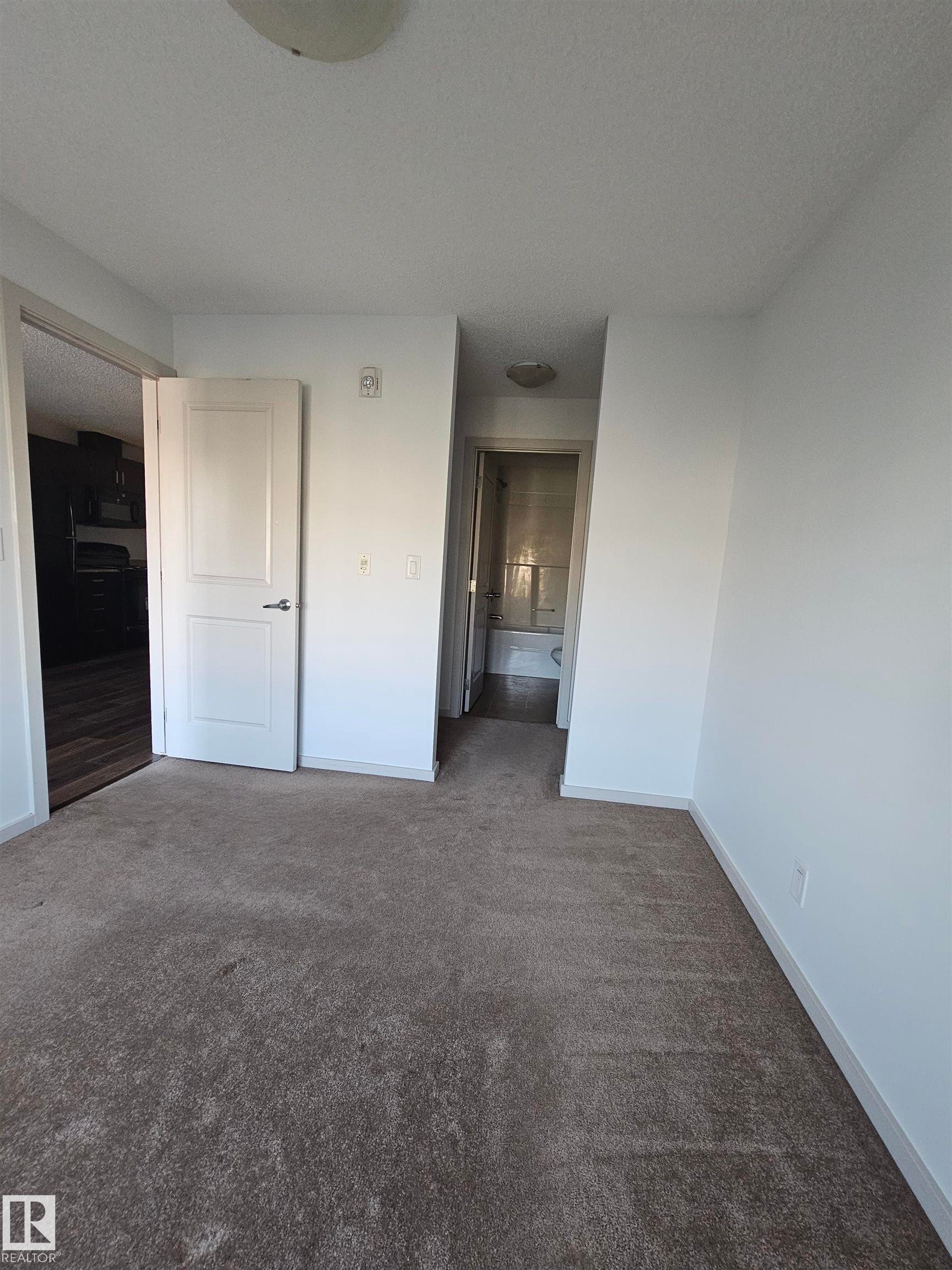Unfurnished bedroom featuring dark carpet and a textured ceiling - 413 5521 7 Avenue, Edmonton, AB - Indoor Photo Showing Other Room