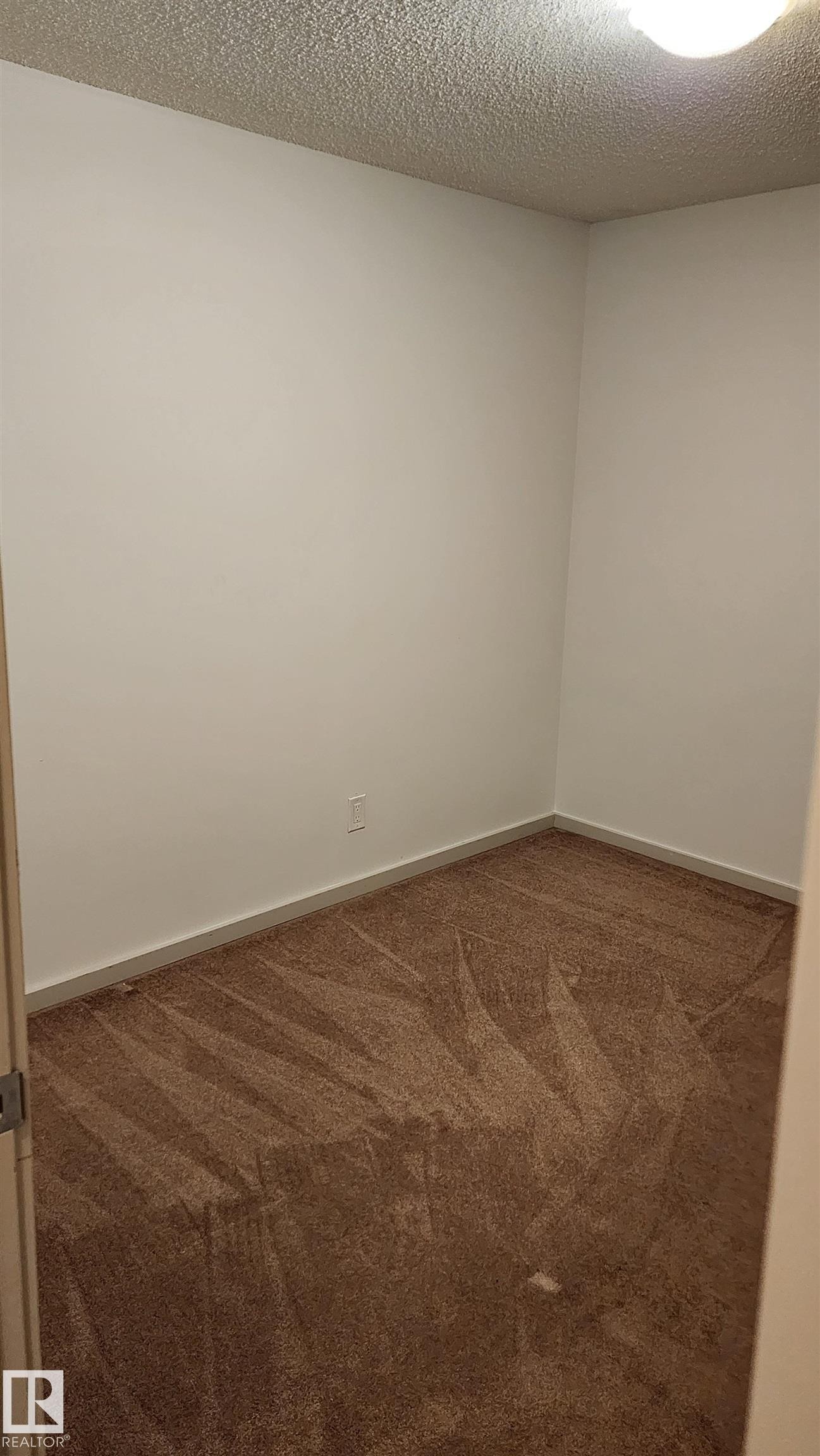 Unfurnished room featuring dark carpet and a textured ceiling - 413 5521 7 Avenue, Edmonton, AB - Indoor Photo Showing Other Room