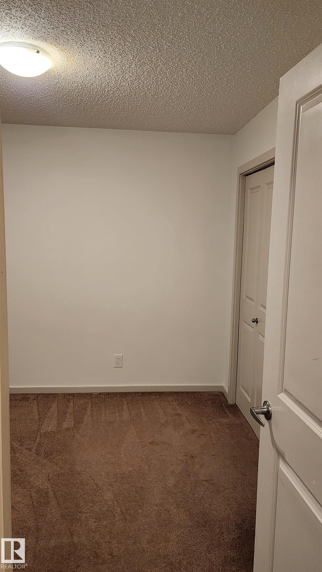 Unfurnished bedroom with a textured ceiling and dark carpet - 413 5521 7 Avenue, Edmonton, AB - Indoor Photo Showing Other Room