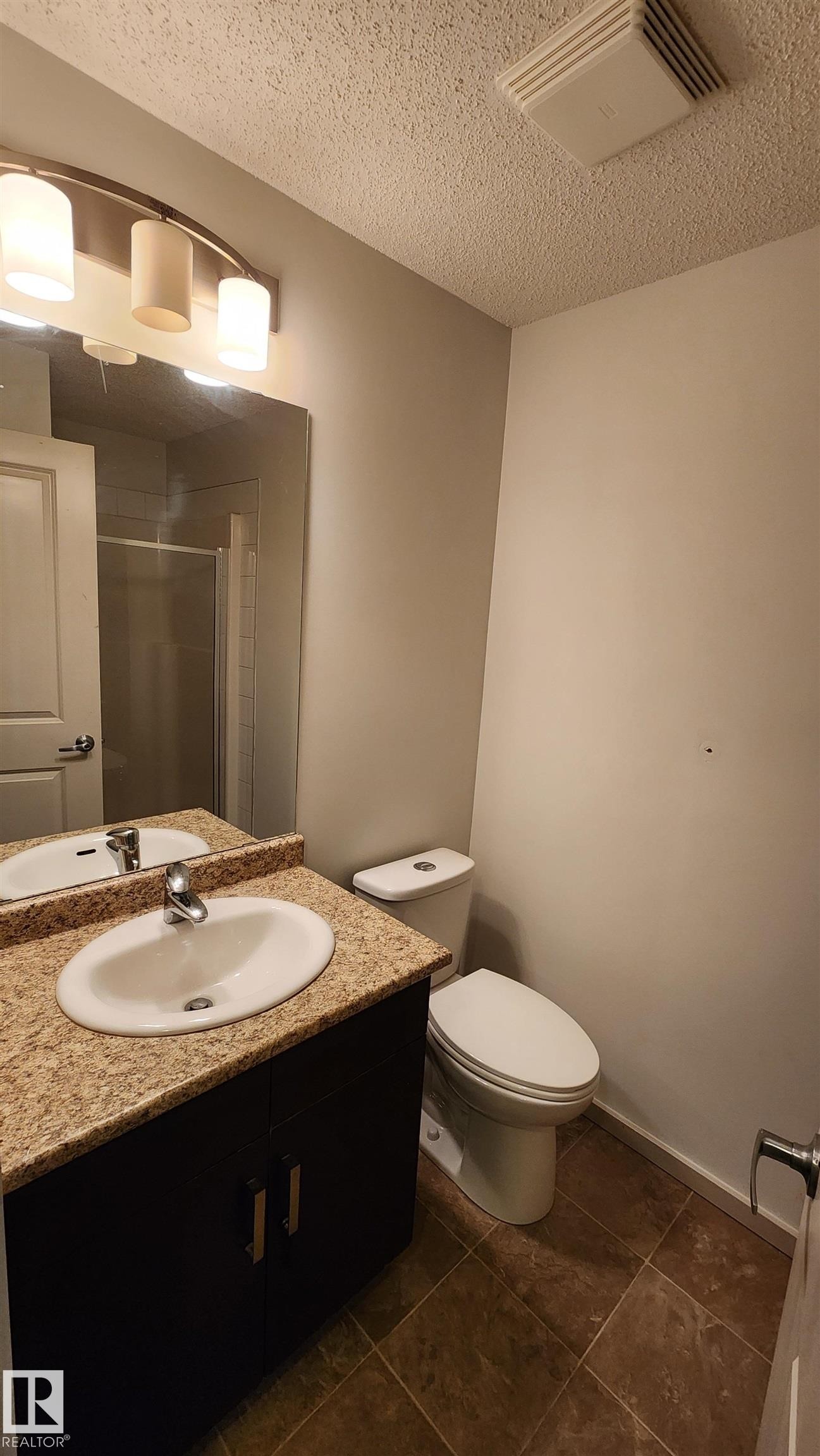 Full bath featuring vanity, a shower stall, a textured ceiling, and dark tile patterned floors - 413 5521 7 Avenue, Edmonton, AB - Indoor Photo Showing Bathroom
