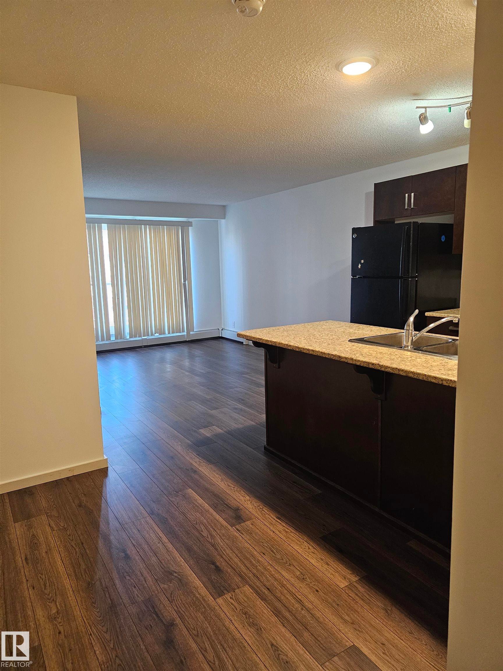 Kitchen with a kitchen bar, freestanding refrigerator, dark wood finish cabinets, dark wood finished floors, and a textured ceiling - 413 5521 7 Avenue, Edmonton, AB - Indoor