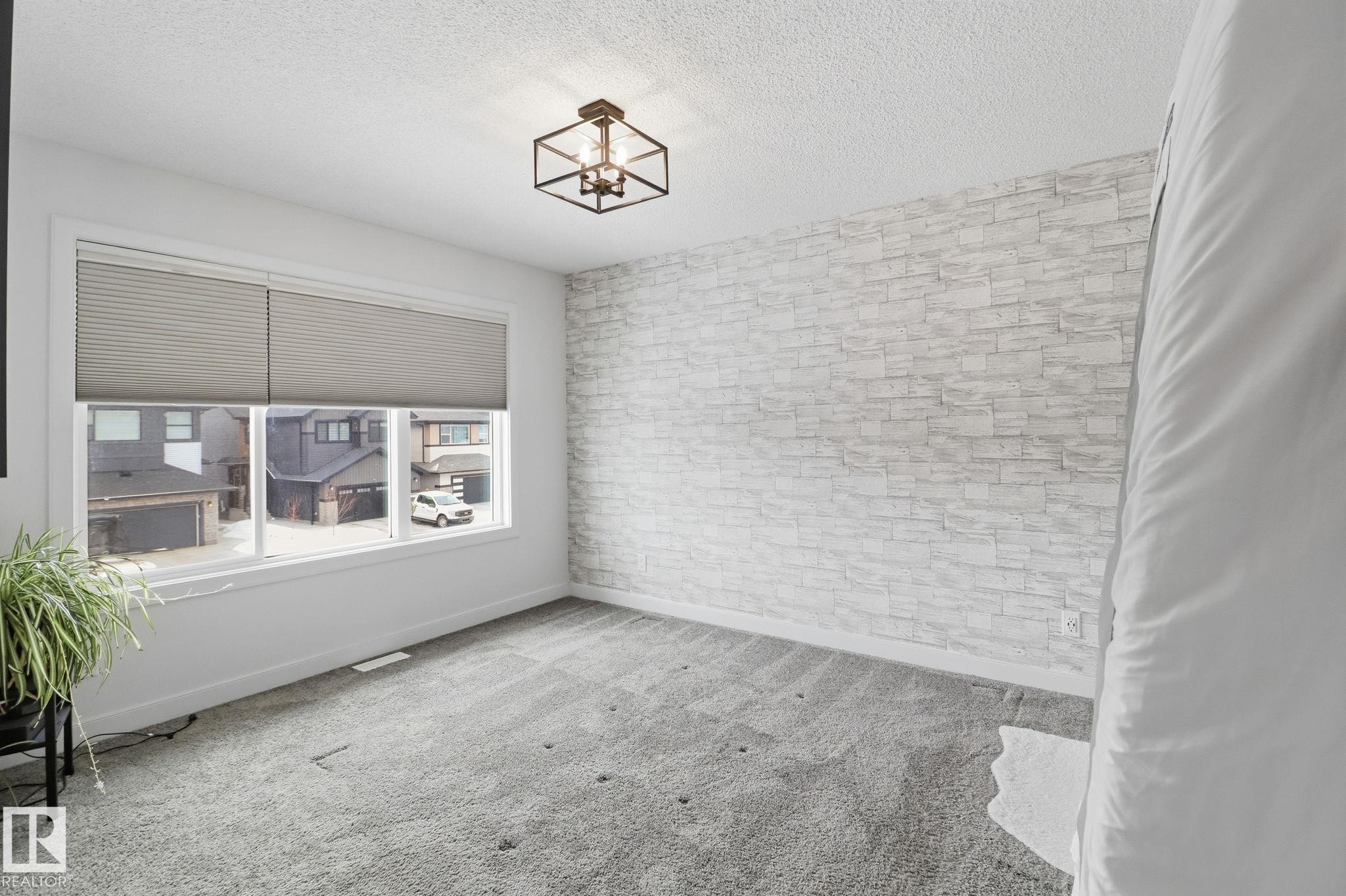 Empty room with light carpet, a textured ceiling, a chandelier, and an accent wall - 3234 Chernowski Way, Edmonton, AB - Indoor Photo Showing Other Room