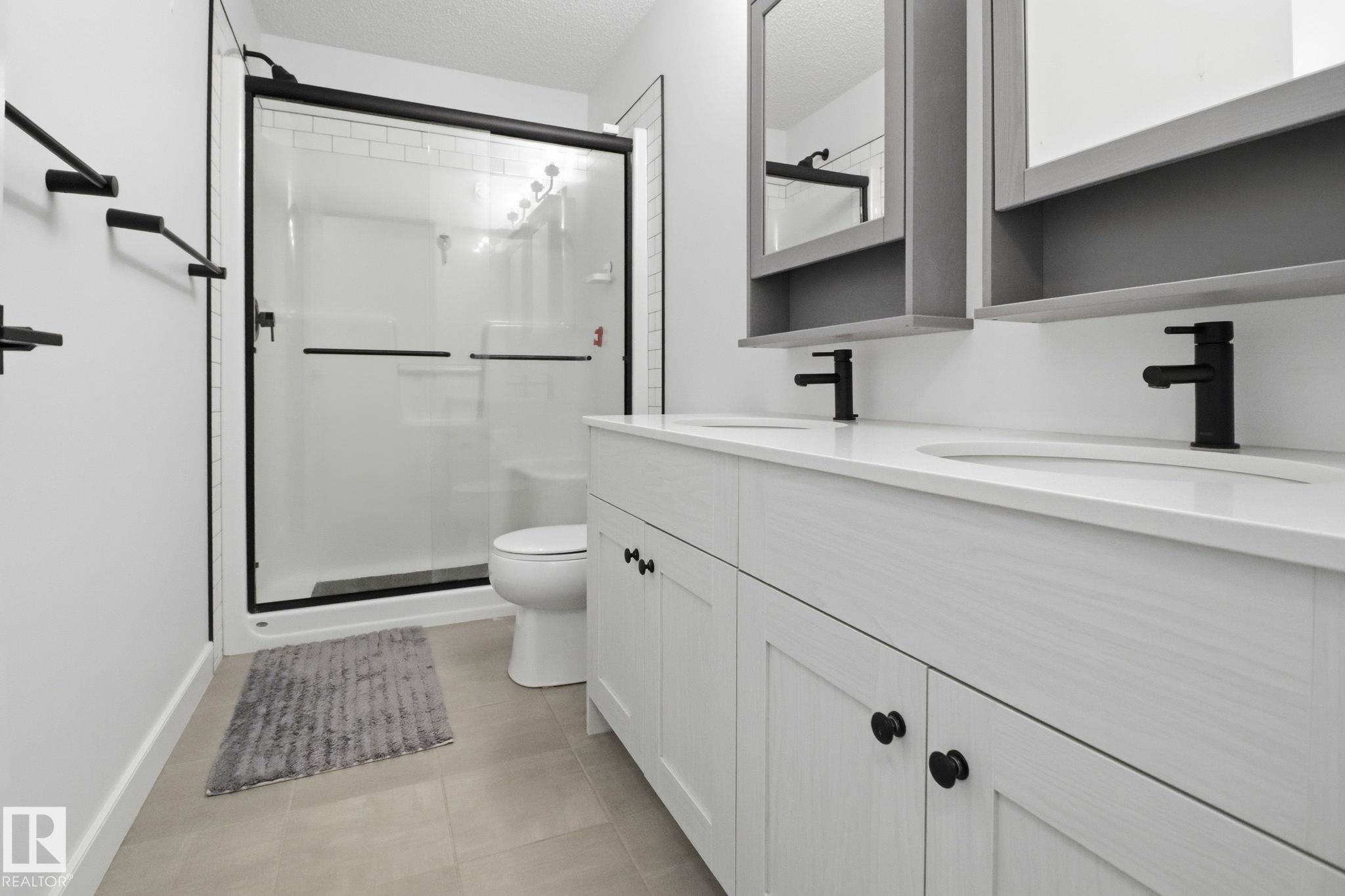 Full bath featuring double vanity, a shower stall, a textured ceiling, and light tile patterned flooring - 3234 Chernowski Way, Edmonton, AB - Indoor Photo Showing Bathroom