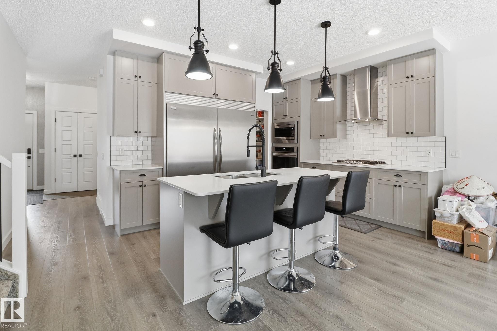 Kitchen with gray cabinets, a kitchen breakfast bar, built in appliances, an island with sink, and light wood finished floors - 3234 Chernowski Way, Edmonton, AB - Indoor Photo Showing Kitchen With Stainless Steel Kitchen With Upgraded Kitchen