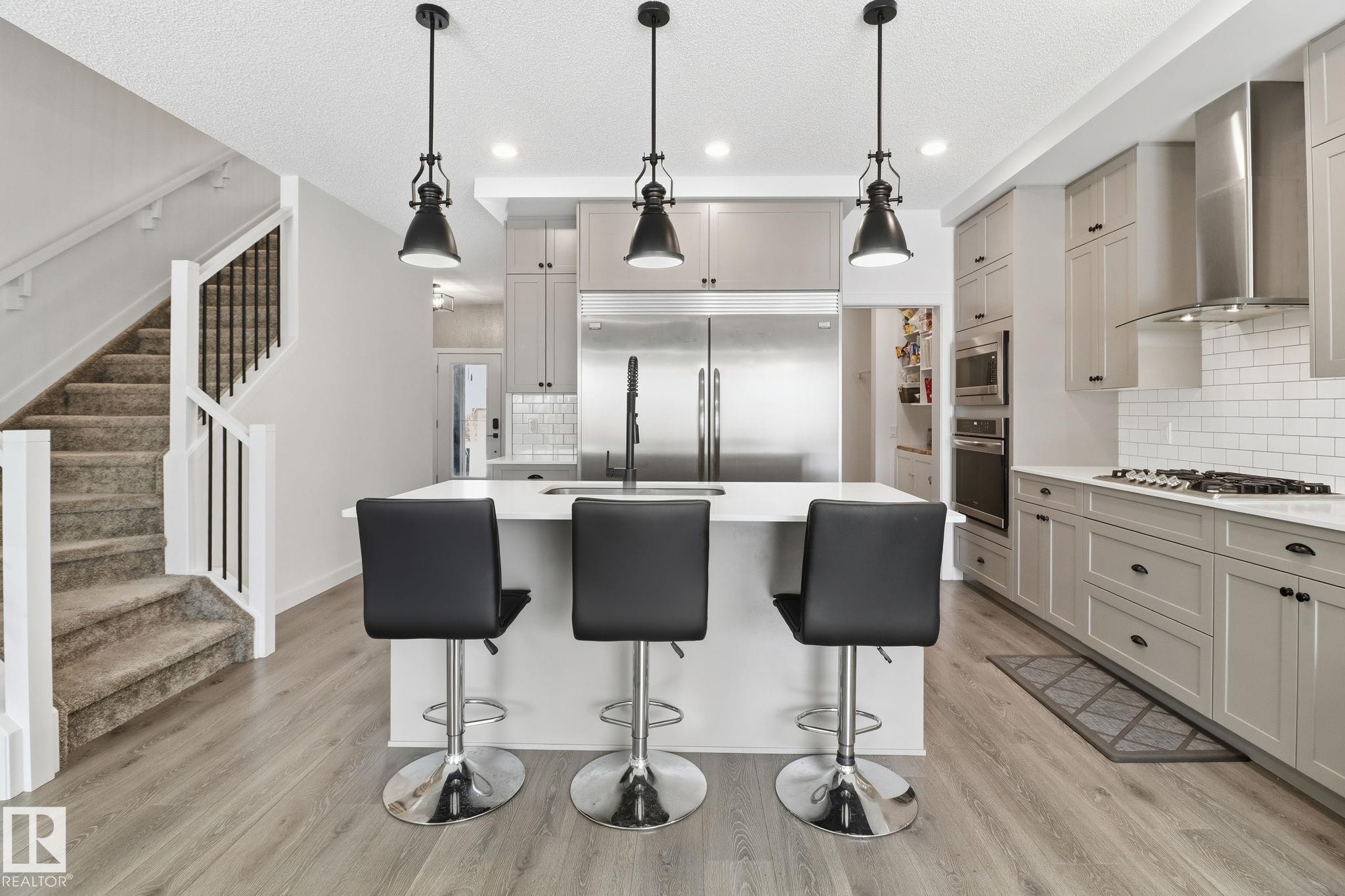 Kitchen with built in appliances, a kitchen island with sink, light wood-style flooring, decorative backsplash, and gray cabinets - 3234 Chernowski Way, Edmonton, AB - Indoor Photo Showing Kitchen With Stainless Steel Kitchen With Upgraded Kitchen