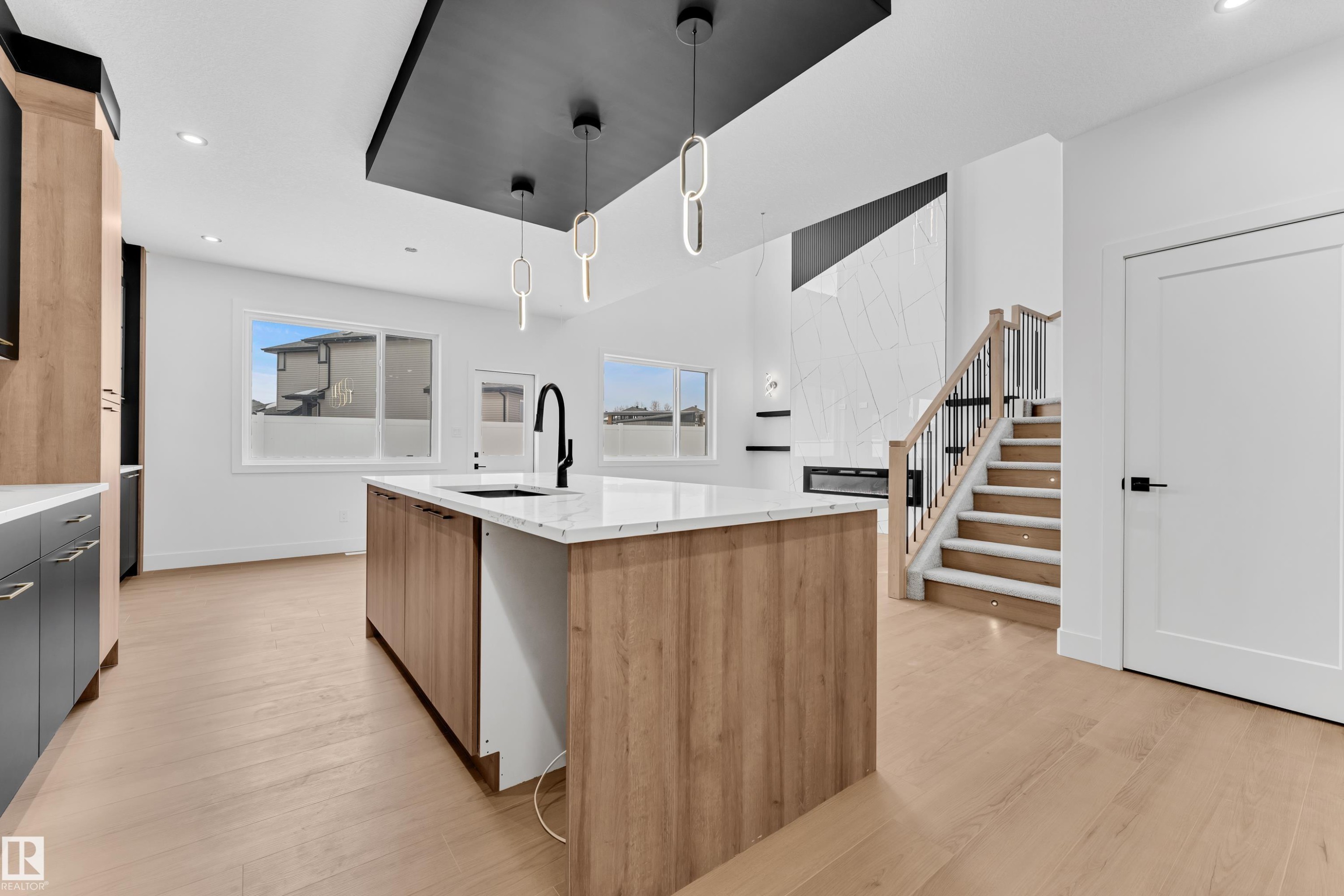 Kitchen featuring a center island with sink, hanging light fixtures, light stone countertops, light wood finished floors, and dual tone cabinetry - 741 Astoria Way, Devon, AB - Indoor Photo Showing Kitchen