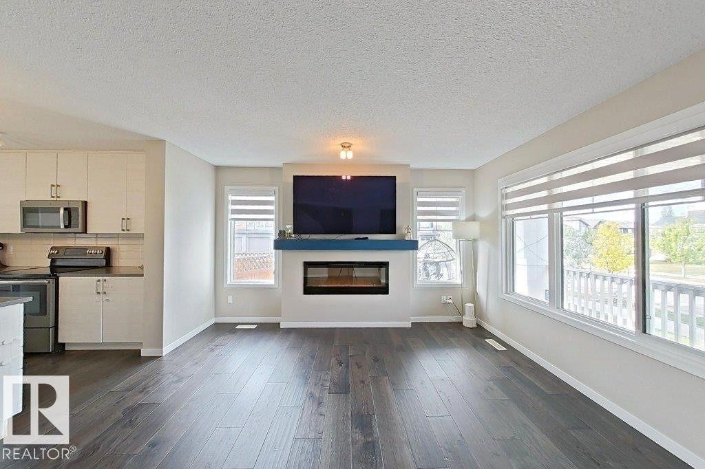 Unfurnished living room featuring dark wood-style floors, a textured ceiling, and a glass covered fireplace - 4303 Prowse Link, Edmonton, AB - Indoor With Fireplace