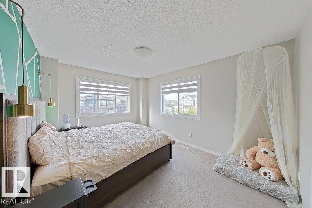 Carpeted bedroom featuring a textured ceiling and multiple windows - 4303 Prowse Link, Edmonton, AB - Indoor Photo Showing Bedroom