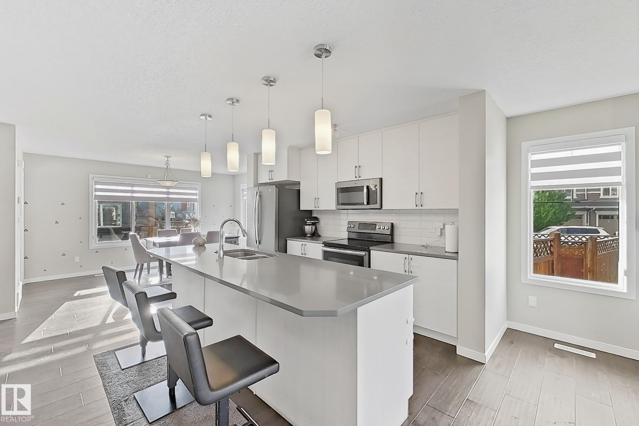Kitchen featuring stainless steel appliances, white cabinets, light wood finished floors, and decorative light fixtures - 4303 Prowse Link, Edmonton, AB - Indoor Photo Showing Kitchen With Double Sink With Upgraded Kitchen