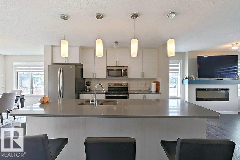 Kitchen featuring dark wood-style floors, stainless steel appliances, hanging light fixtures, and tasteful backsplash - 4303 Prowse Link, Edmonton, AB - Indoor Photo Showing Kitchen With Double Sink With Upgraded Kitchen