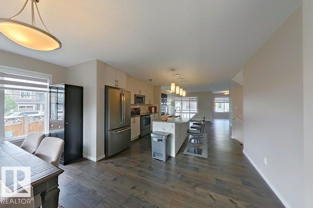 Kitchen with pendant lighting, stainless steel appliances, a breakfast bar area, a kitchen island with sink, and dark wood-style flooring - 4303 Prowse Link, Edmonton, AB - Indoor